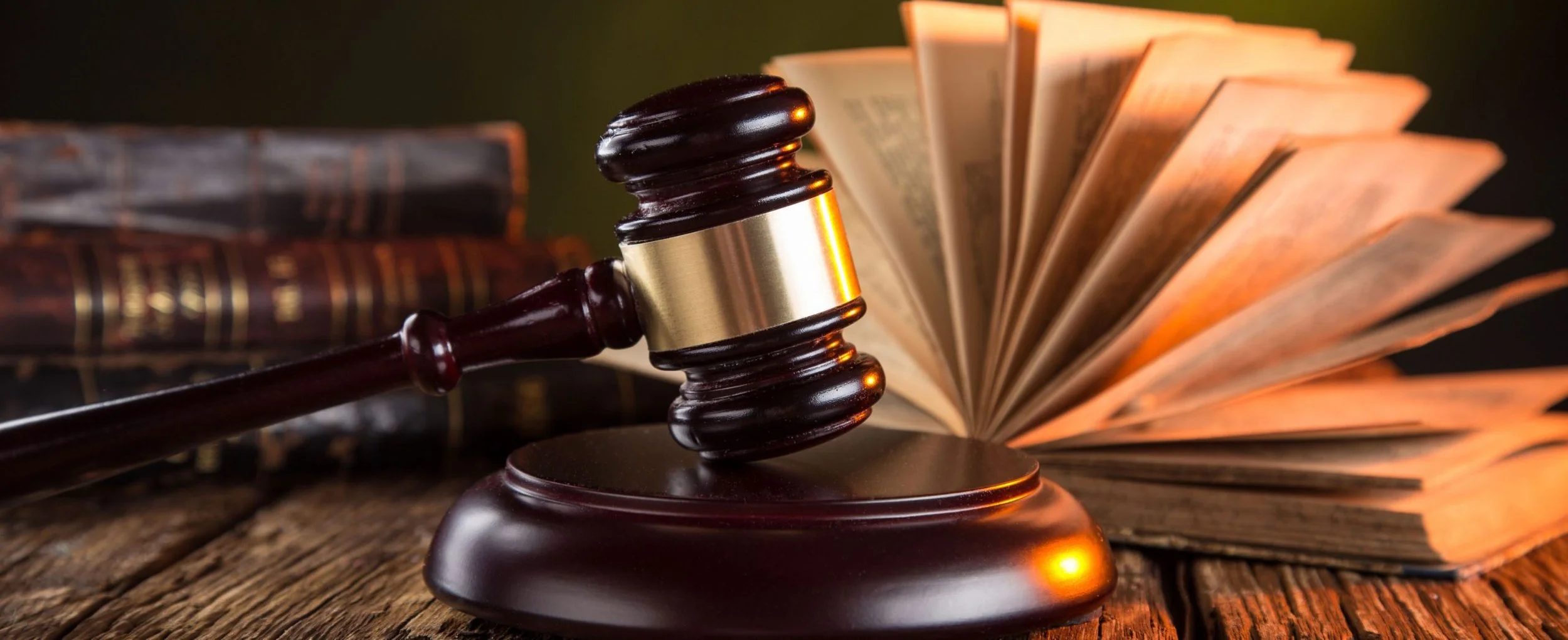 Gavel, open law book, and additional legal books on a wooden surface.