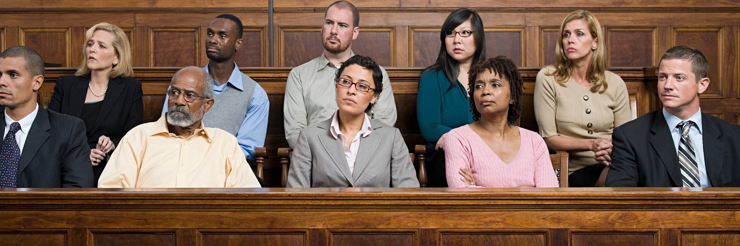A group of eleven diverse adults seated in a courtroom, listening attentively.