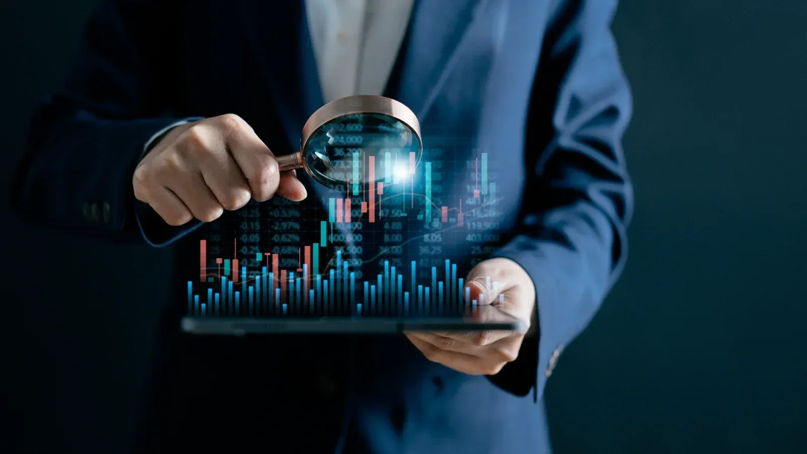 Business person in suit analyzing digital stock market data on tablet with magnifying glass.