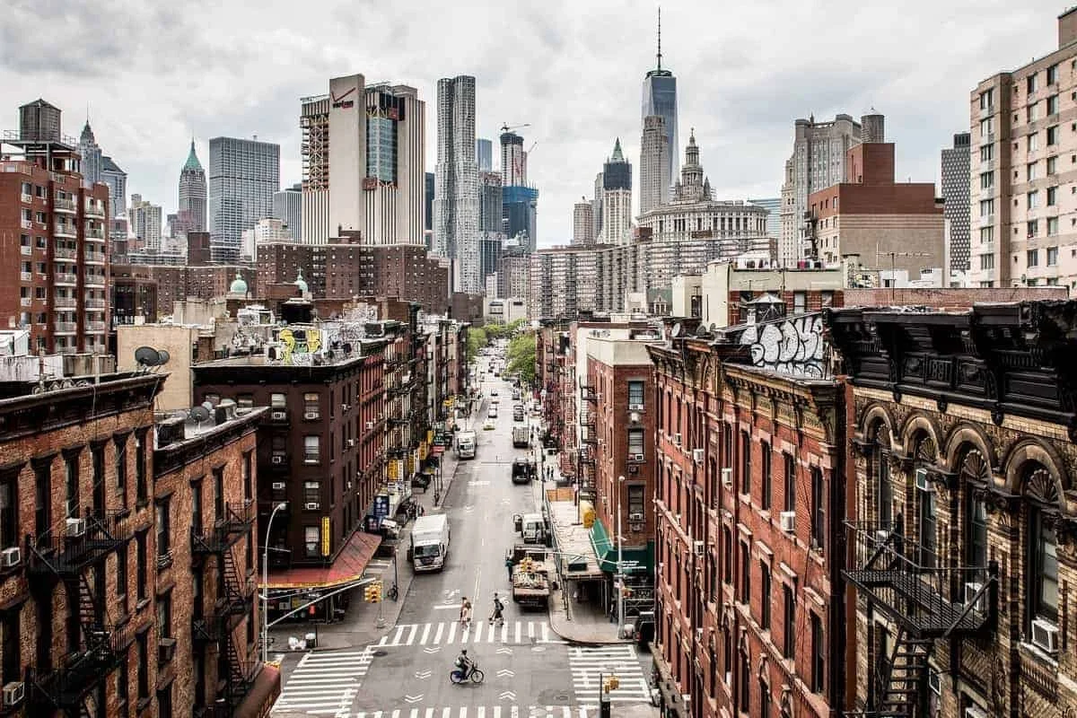 City street scene with brick buildings and skyscrapers in downtown New York City, with cars, trucks, and a cyclist crossing the crosswalk on an overcast day.