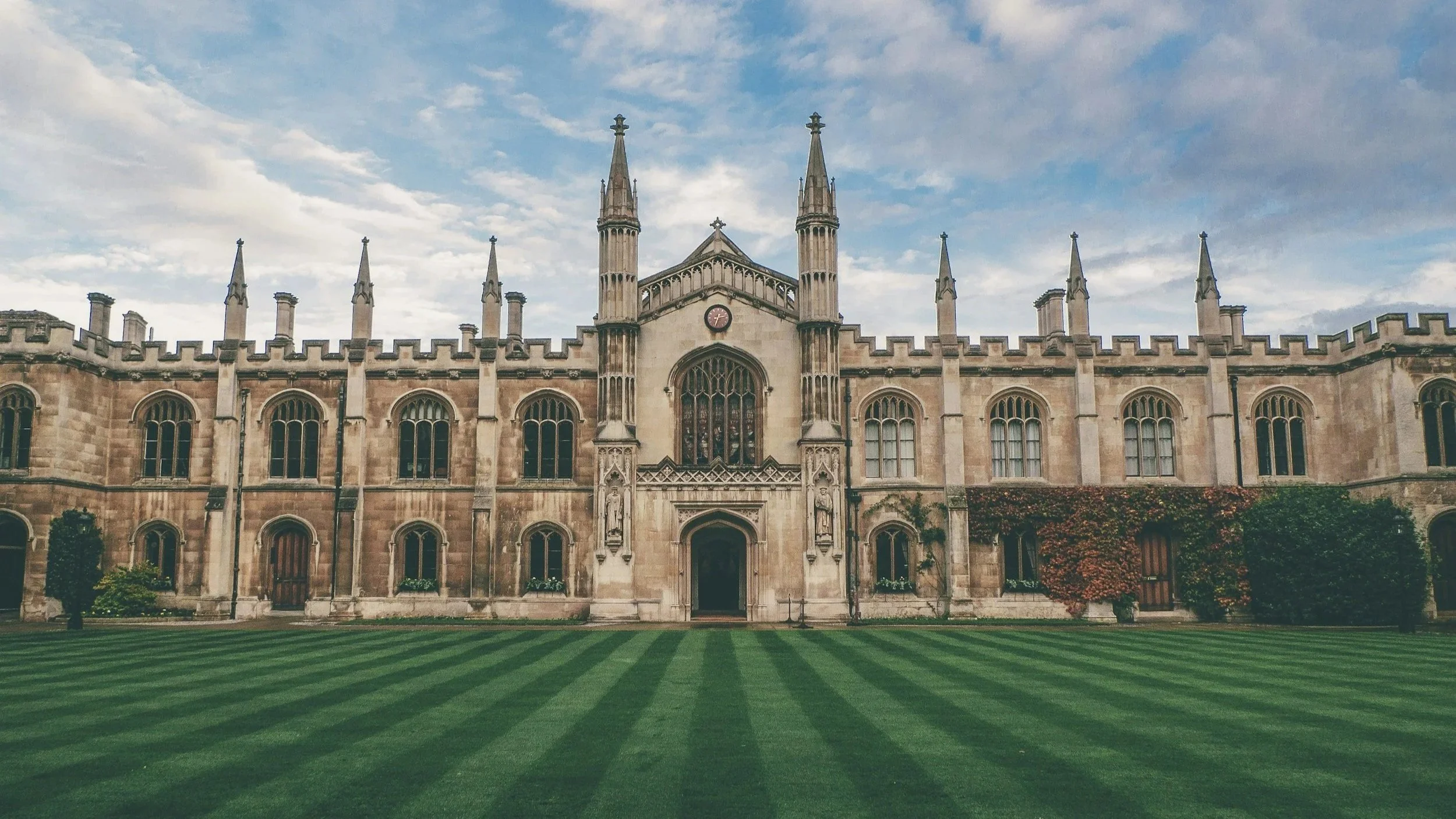 Historical Gothic-style building with tall spires, arched windows, and a well-maintained striped green lawn in front.