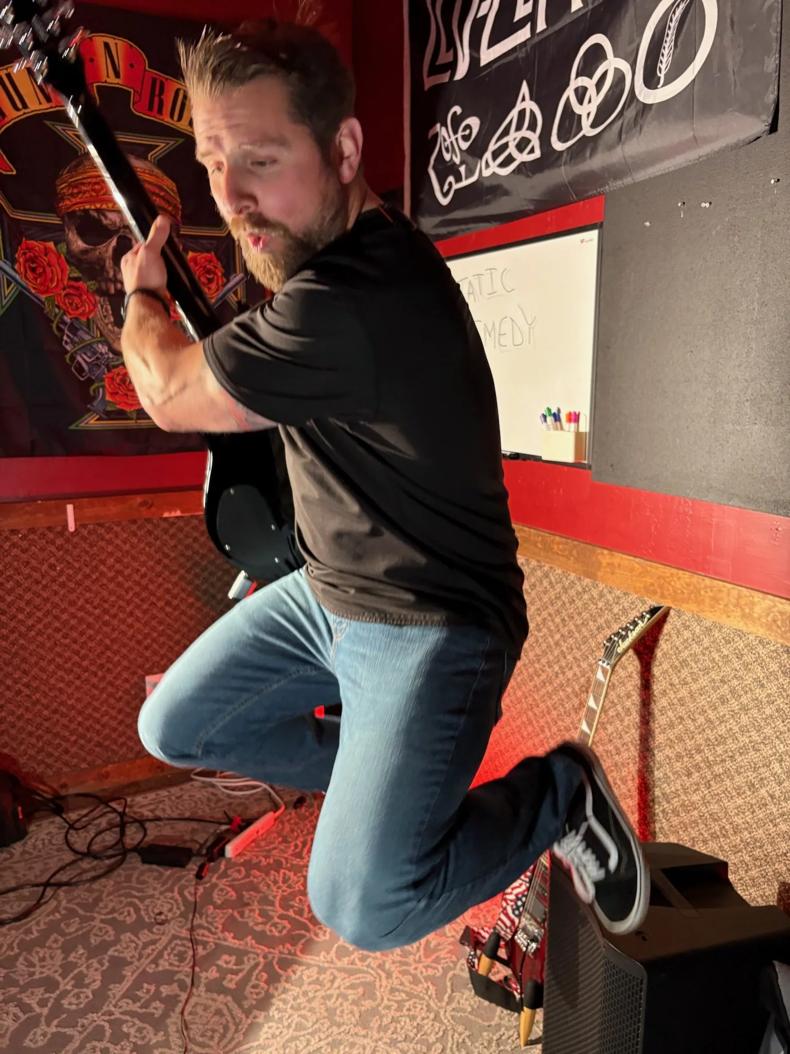 A man playing an electric guitar on stage at Fat Fish Blue, with musical equipment and a sign in the background.