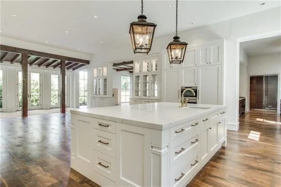 Modern kitchen with white cabinets and large island,  rustic pendant lighting, alder wood floors and rustic wood beam ceiling detail, pass through to butler panty and bar.