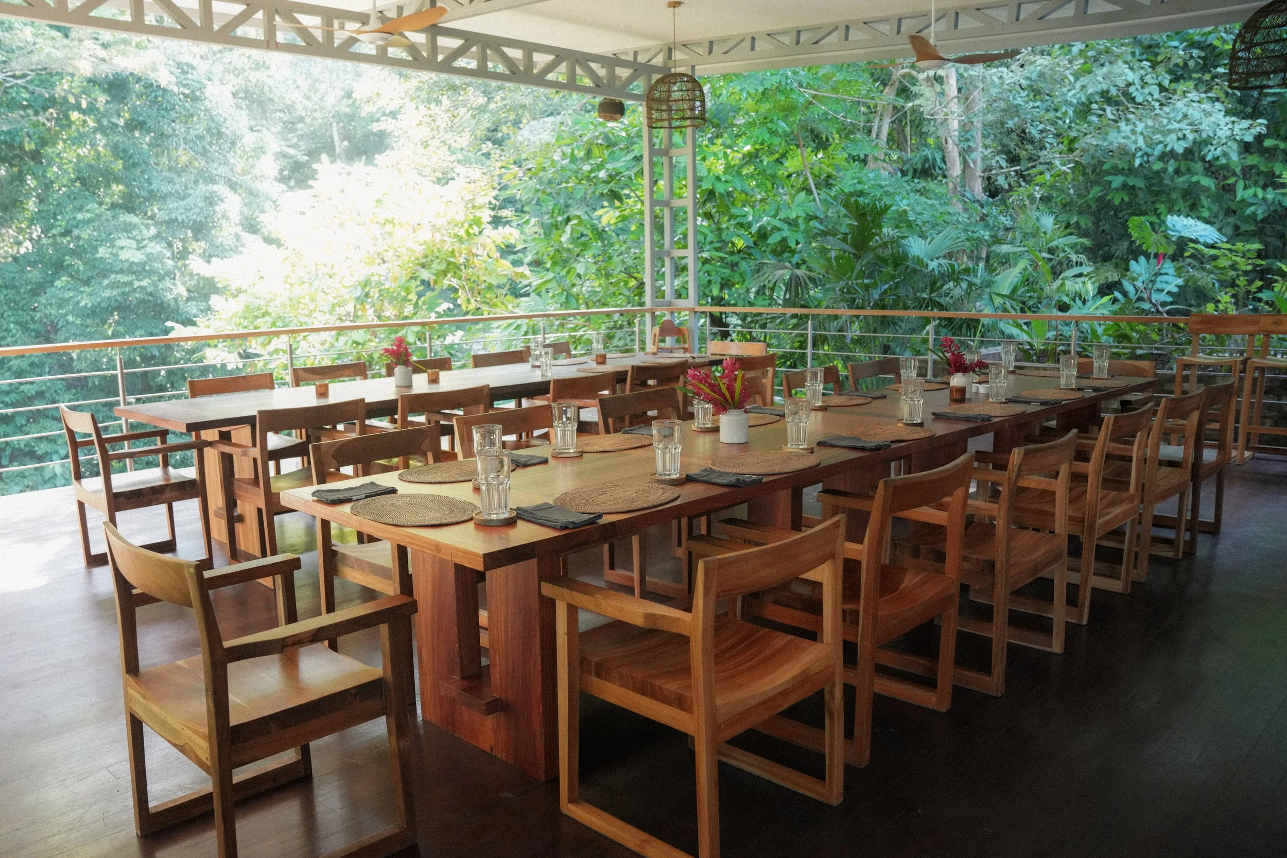 Outdoor dining area of a restaurant with wooden tables and chairs arranged on a deck, surrounded by a pleasant ambiance.