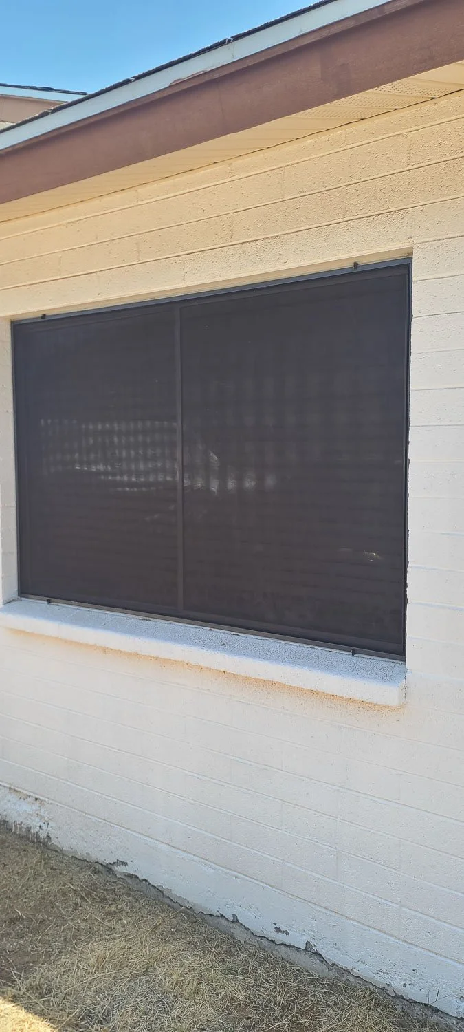 Exterior view of a house with a screened-in window, white brick wall, and a brown roof.