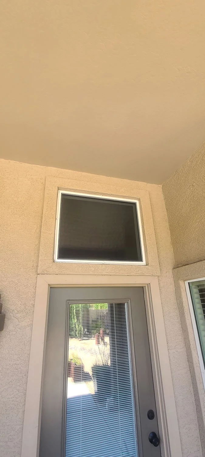 The image shows a beige stucco wall with a door that has vertical blinds and a small window above it with dark glass, all outdoors.