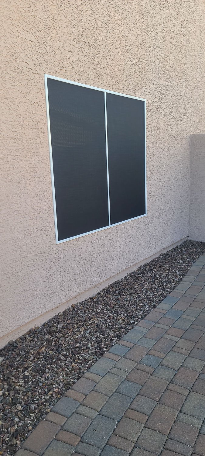 Solar panels mounted on a beige stucco wall beside a walkway with pavers and gravel.