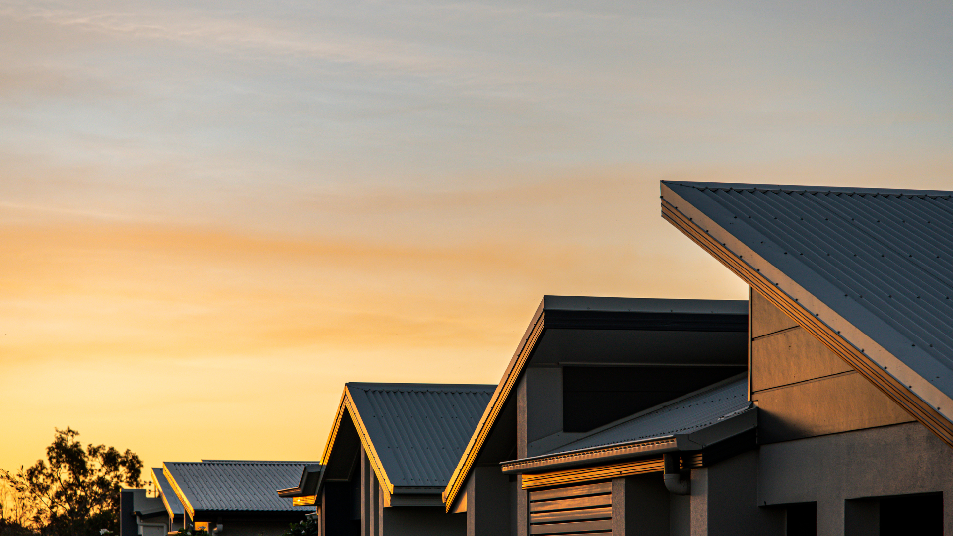 Residential buildings with metal roofs during sunset, with a cloudy sky and trees in the background.