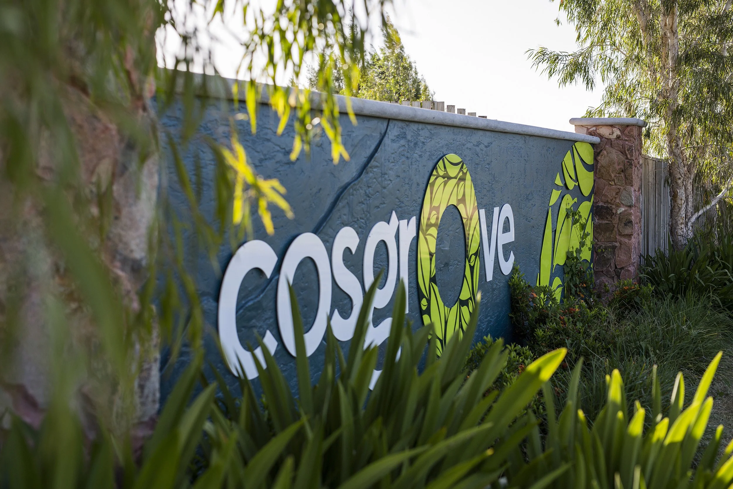 Sign that reads 'escape' with decorative green and yellow circles, surrounded by greenery and trees.