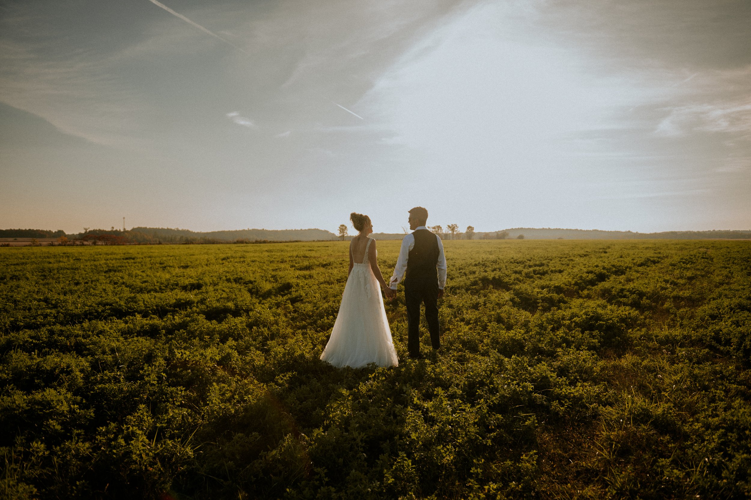 Jeune marié dans un champs au coucher du soleil au beau mois d'Aout se tenant par la main