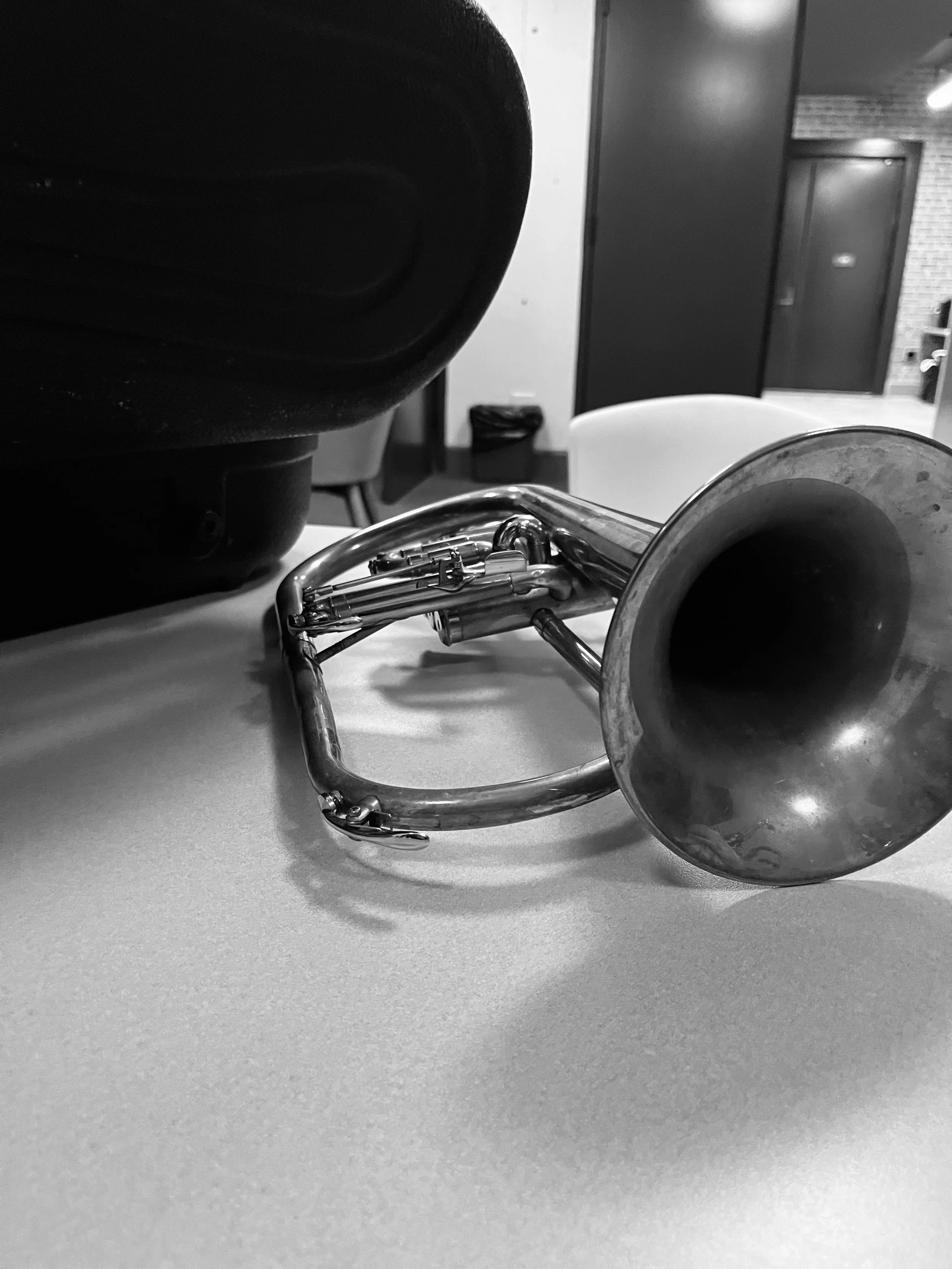 A trumpet lying on a table with a black speaker in the background.