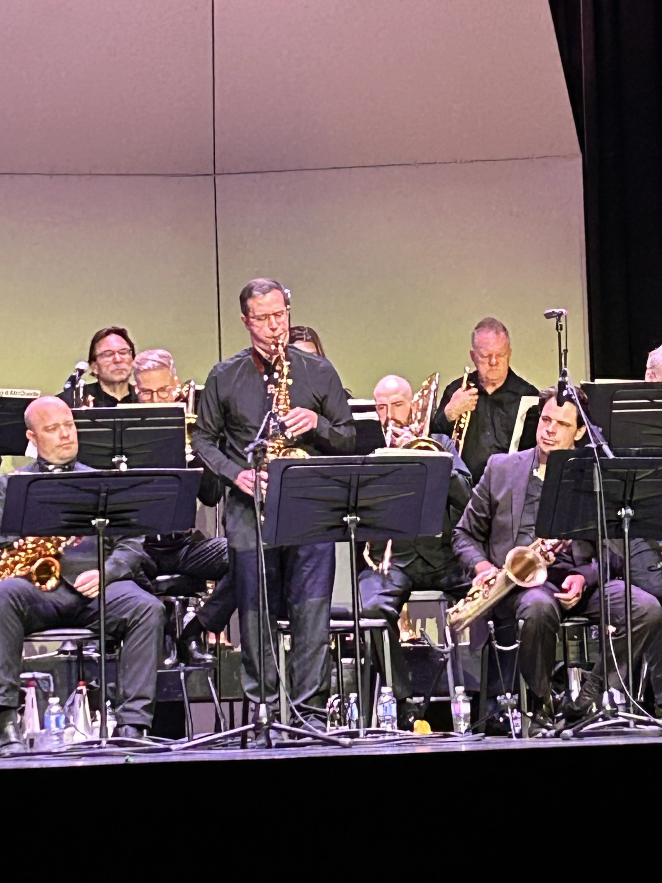 Jazz band performing on stage with musicians playing saxophones, trumpets, and other instruments, and a conductor standing in front.