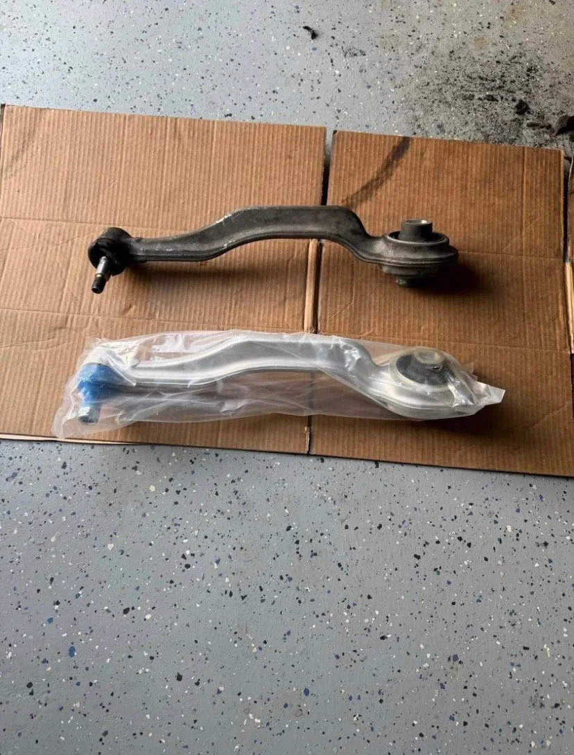 Two car control arms, one used and rusty, the other new and packaged, replaced in a garage.