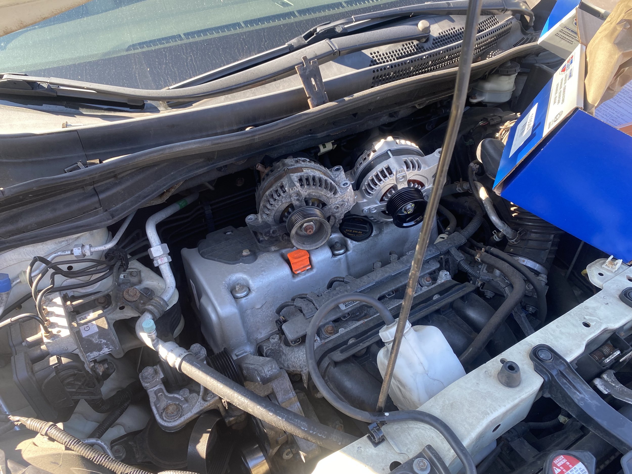 Open car hood revealing engine with alternator and accessory belts.