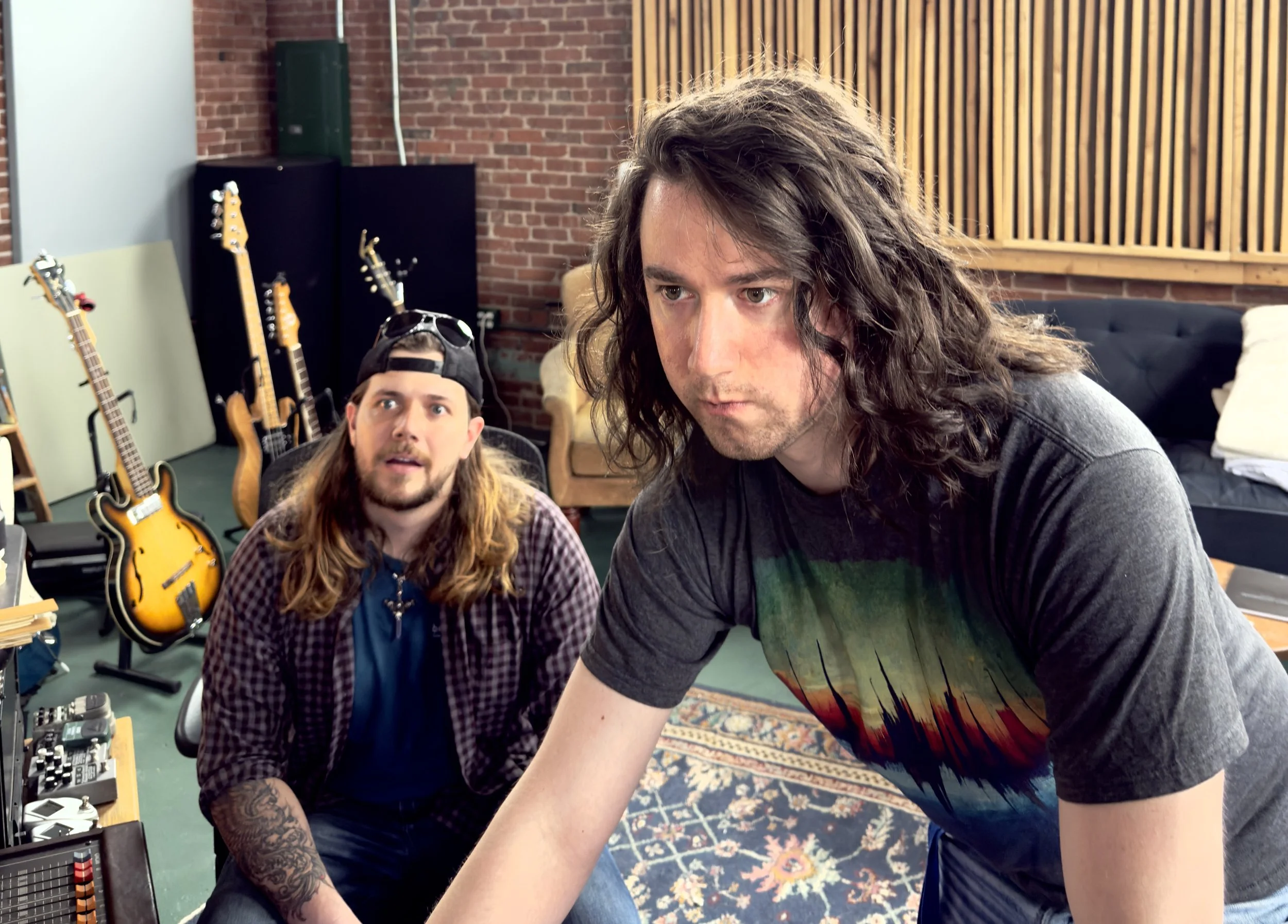Two men in a music studio surrounded by guitars, equipment, and brick walls, with one man with long curly hair and the other with long hair wearing a backward cap, both focused on music production. A recreation of the popular Young Thug meme