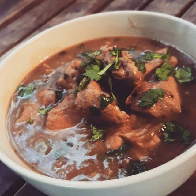 A bowl of beef stew garnished with cilantro, on a wooden surface.