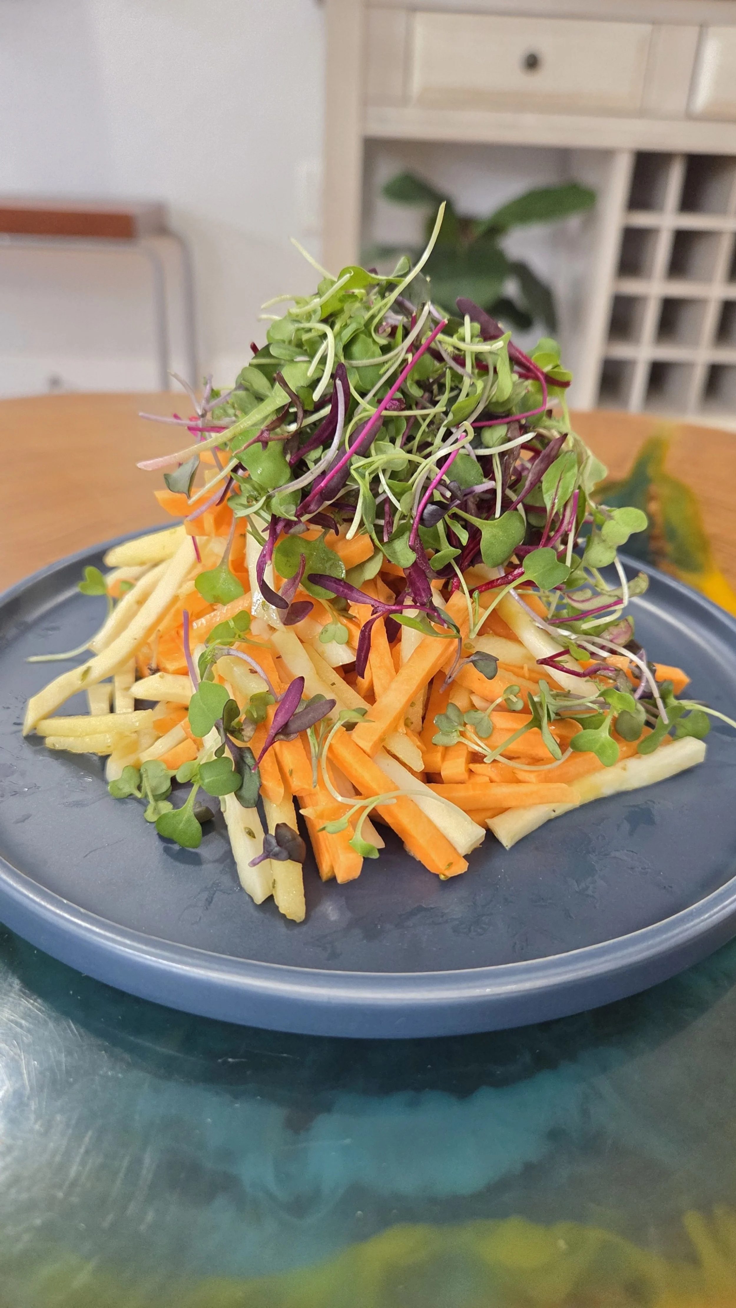 A plate of shredded carrots, jicama, and microgreens on a blue plate.