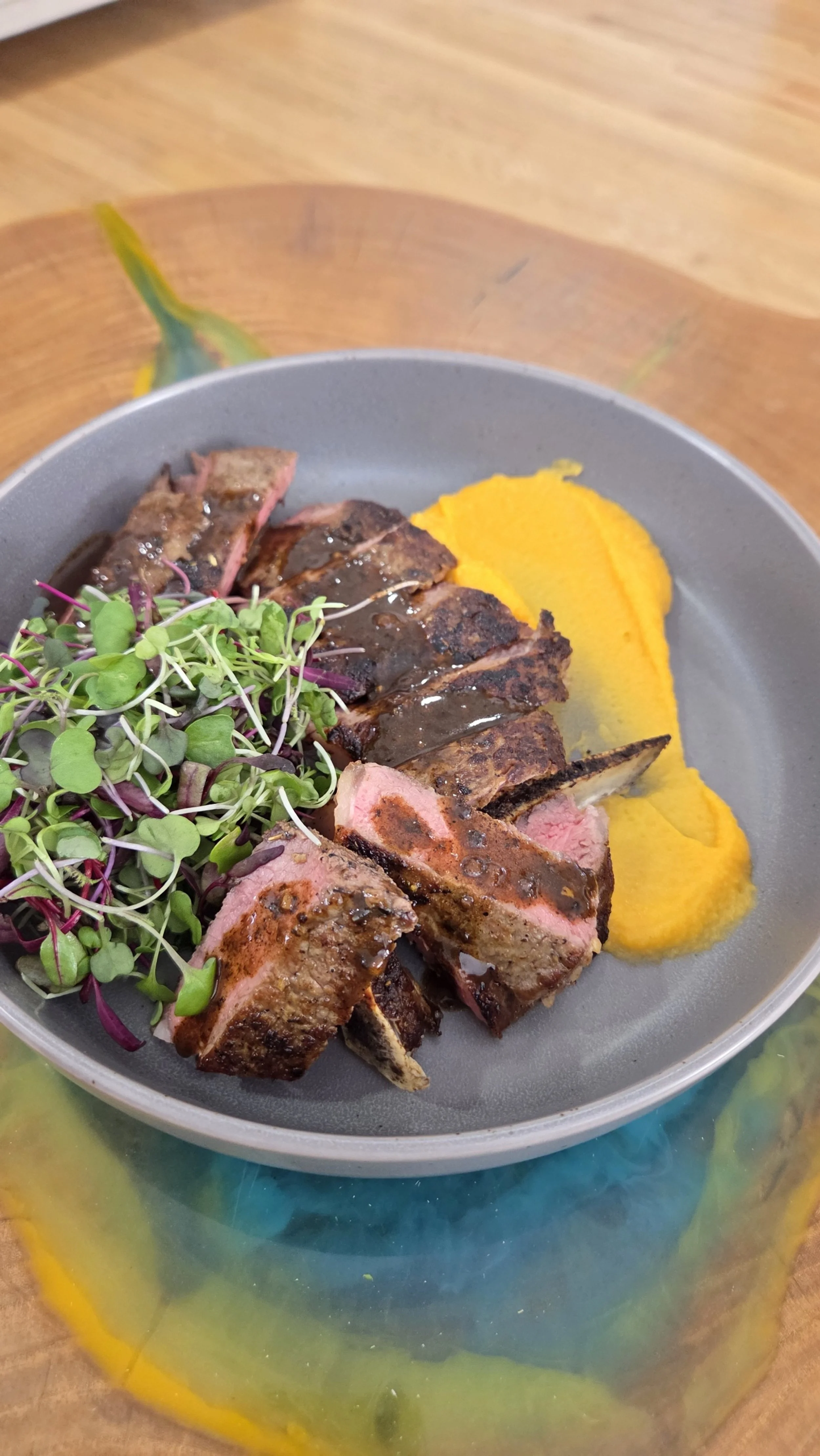 A plate with slices of Seared Steak, a serving of mashed carrots, and microgreens garnishing the steak.