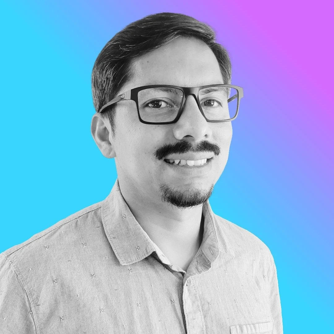 A black and white portrait of a smiling man with glasses, mustache, and goatee, wearing a light-colored collared shirt, with a gradient blue and purple background.