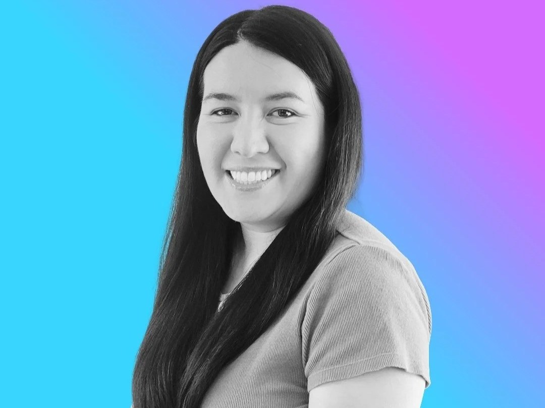 A woman with long dark hair smiling, in a close-up portrait against a colorful gradient background of blue, purple, and pink.