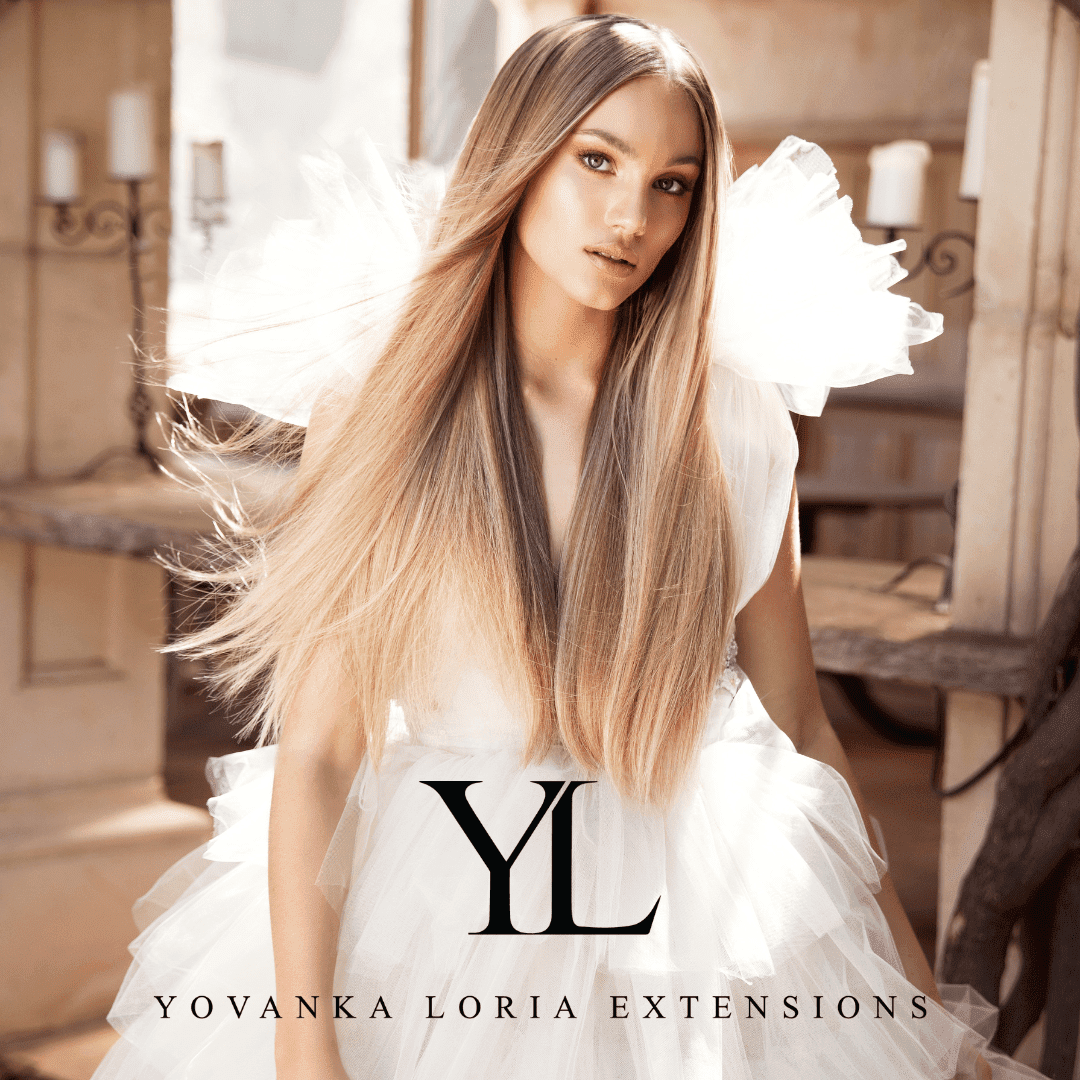 A woman with long, straight, blonde hair wearing an elegant white dress with large ruffled shoulders, standing in a rustic wooden interior. weft hair extension