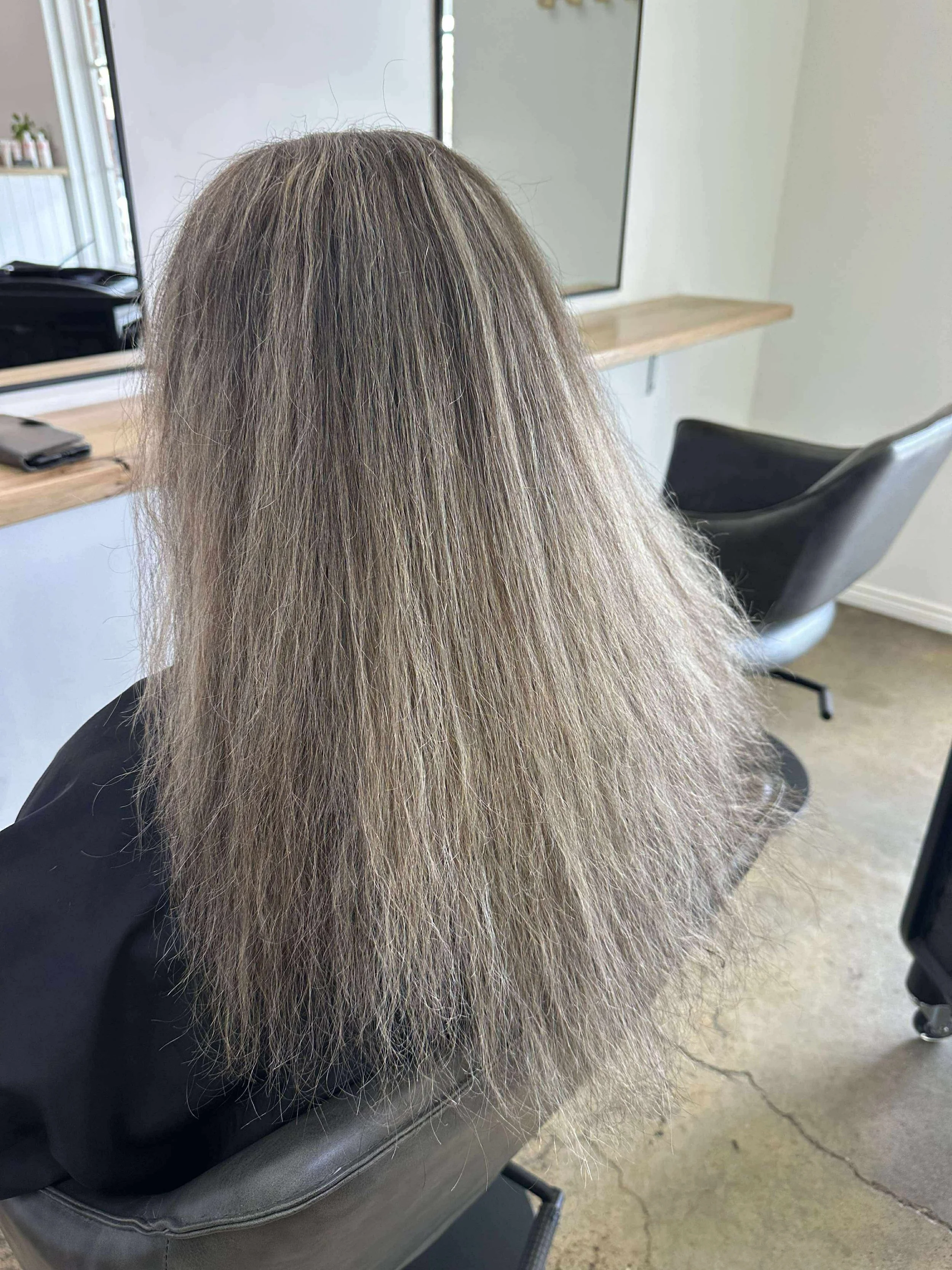 Woman with long, gray, frizzy hair sitting in a salon chair. before keratin treatment
