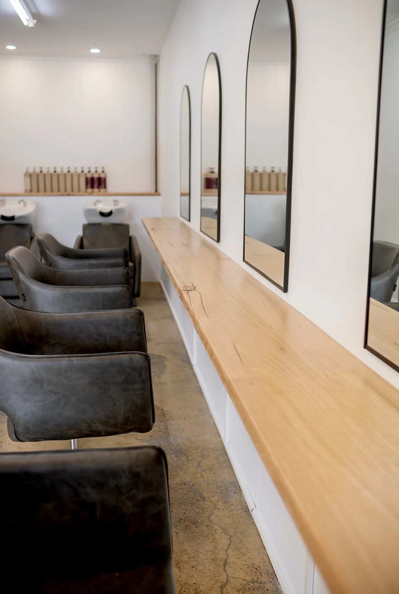 Interior of a hair salon with black chairs, mirrors, and a wooden counter along the wall.