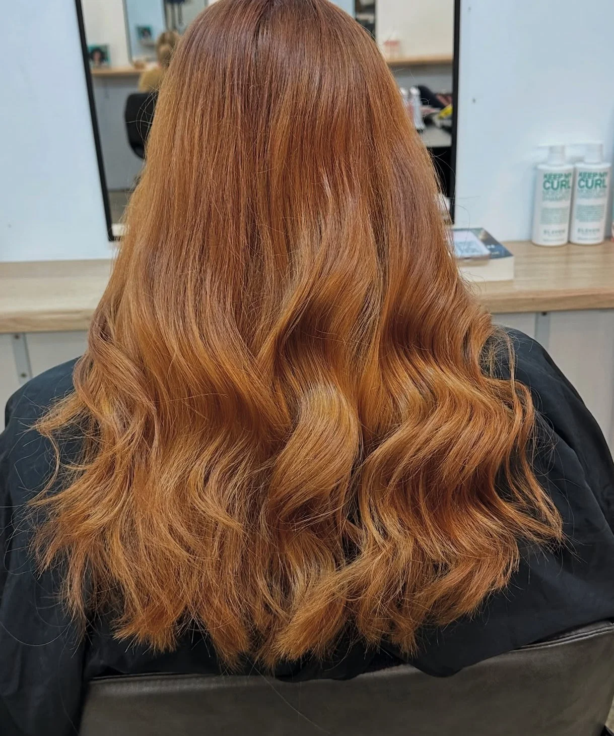 Back view of a woman with long, wavy, red hair in a salon