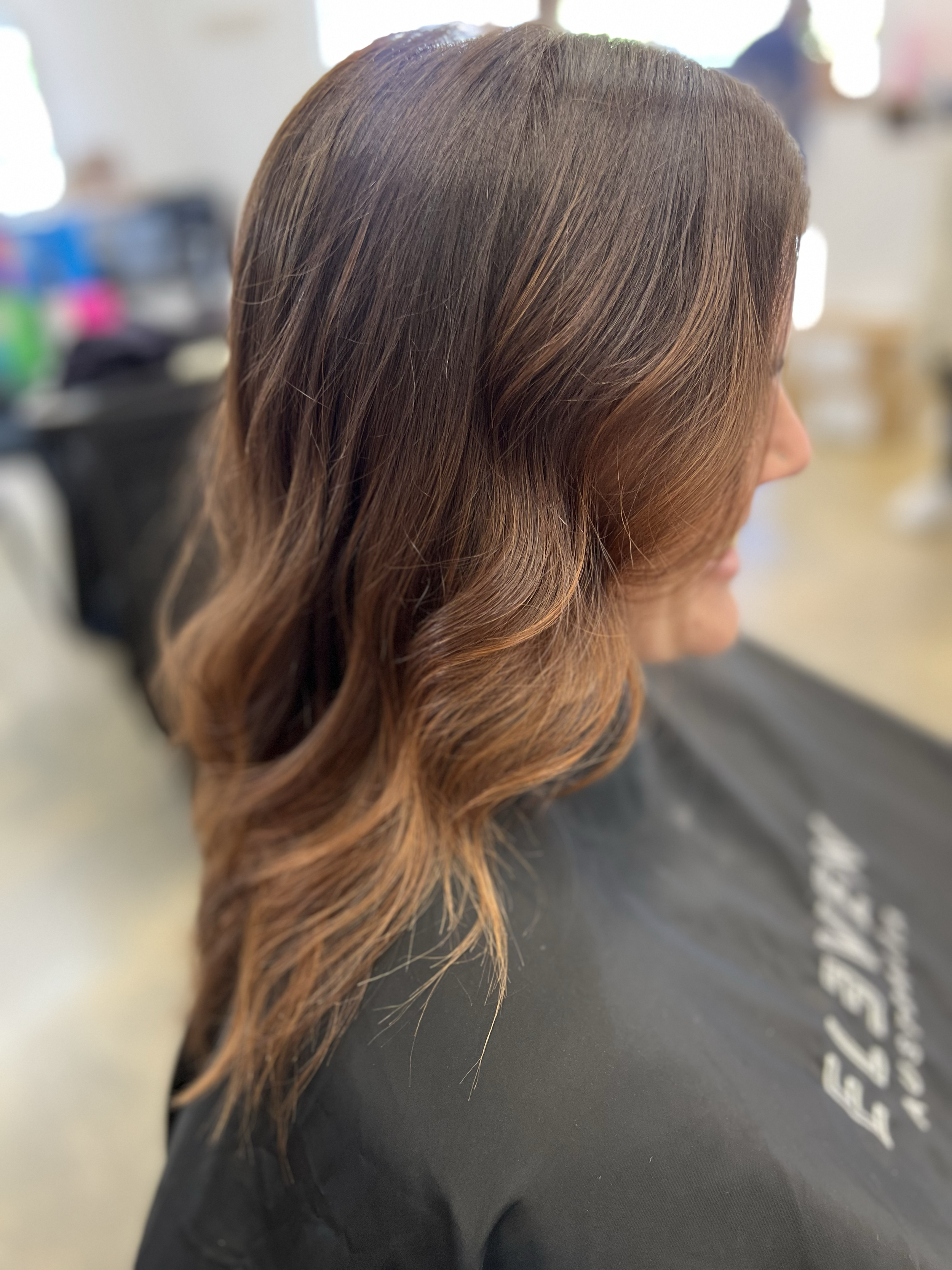 Side view of a woman with wavy, medium-length brown hair in a salon chair.
