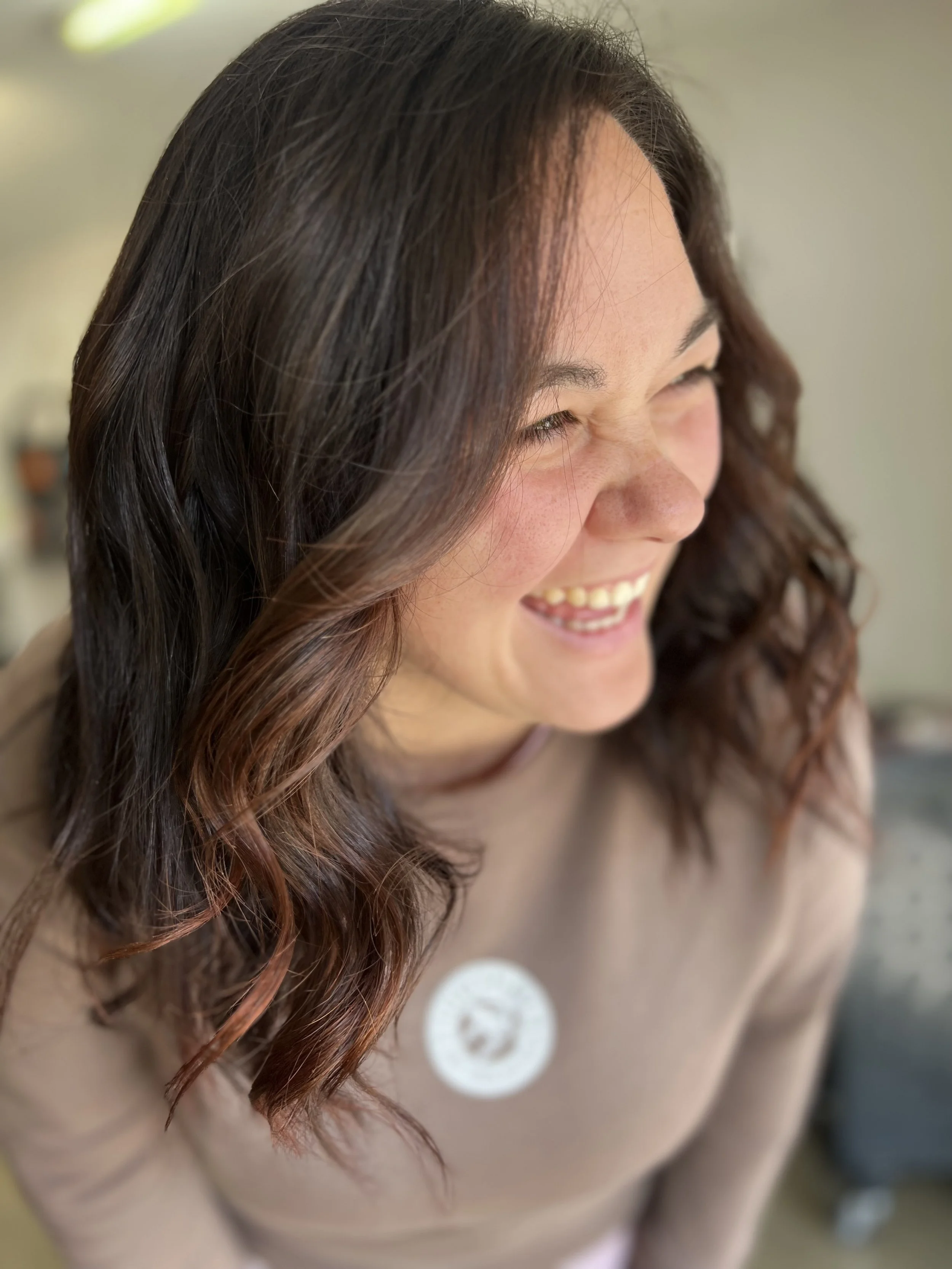 A woman with long, wavy brown hair smiling and laughing.
