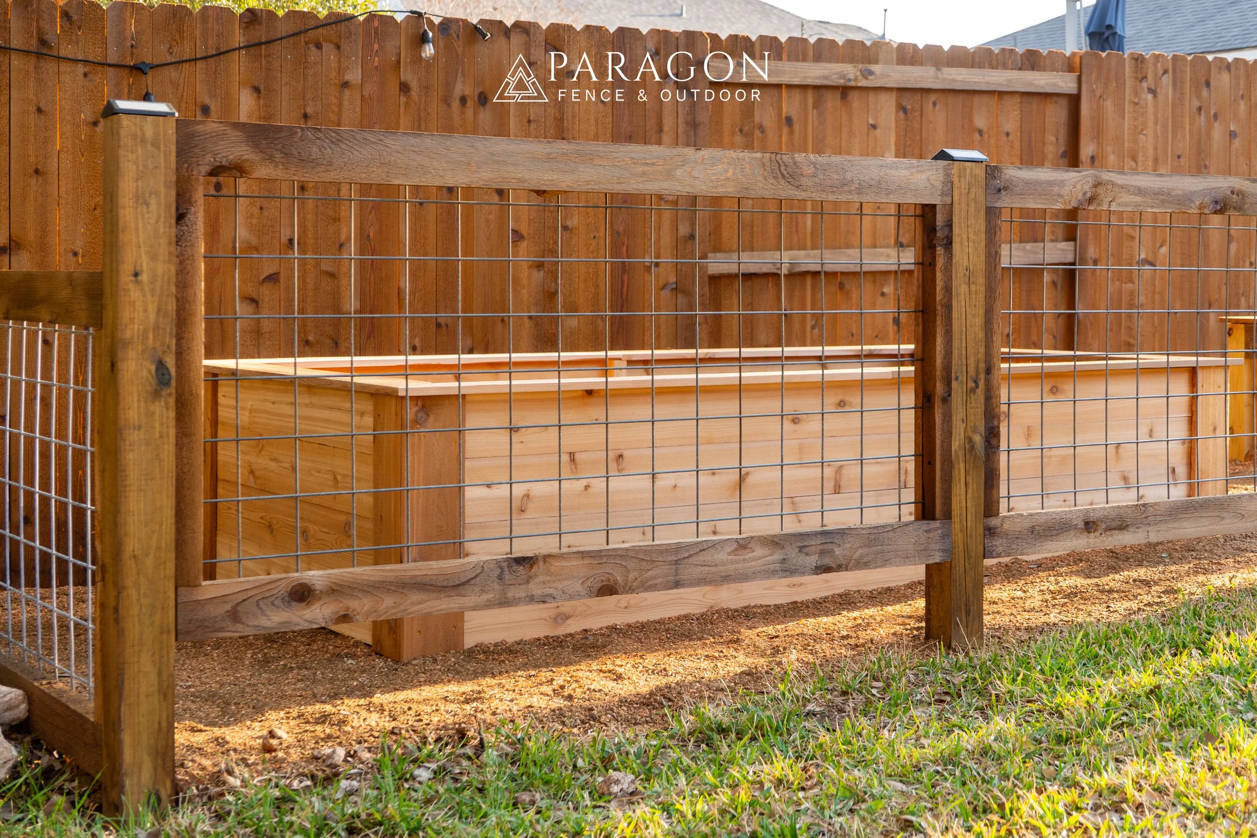 Wooden raised garden bed with wire fencing in a backyard, with a wooden fence and grass in the background.
