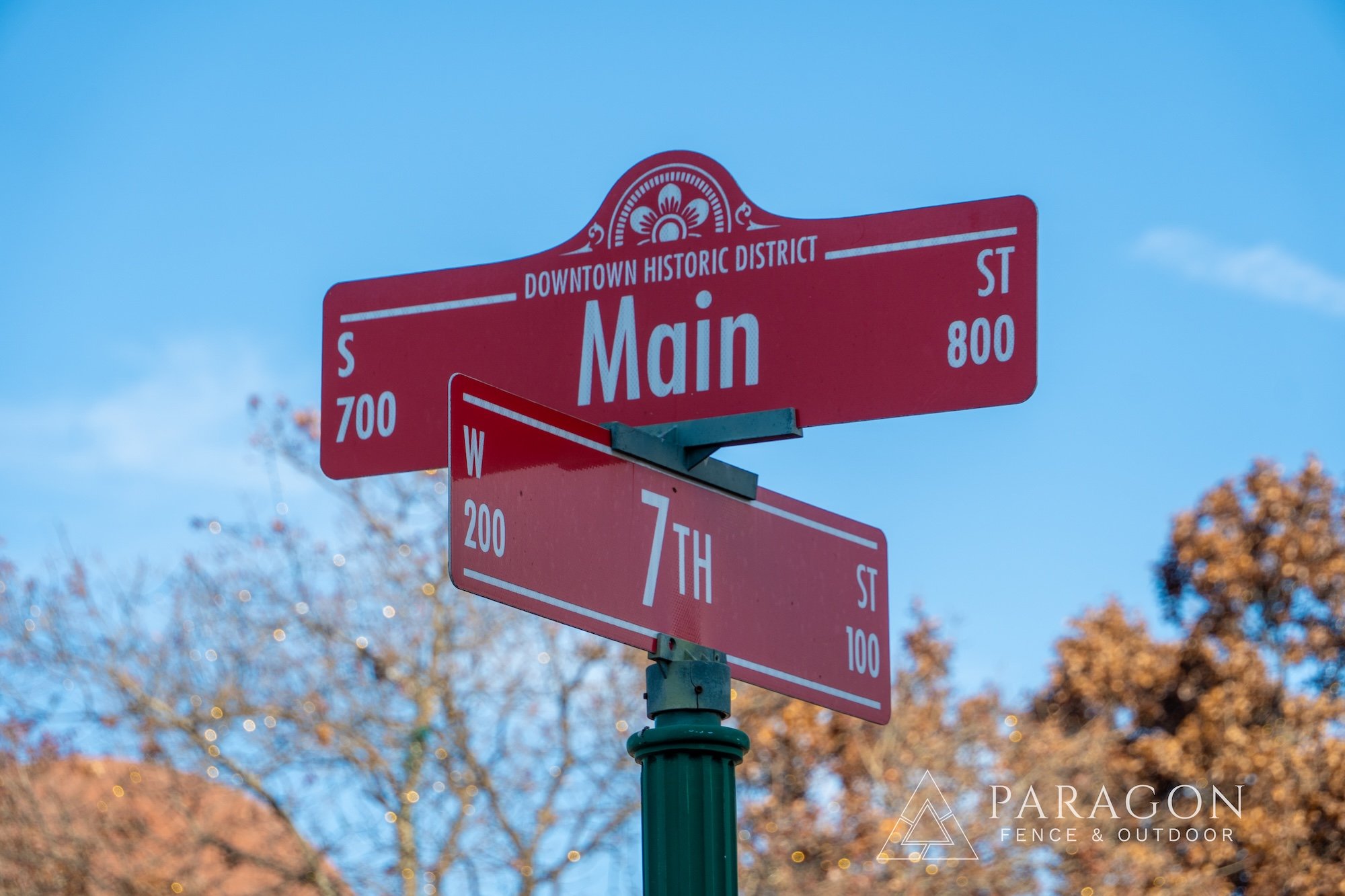 Street signs at intersection of Main Street and 7th Street in downtown historic district, with a blue sky and autumn trees in the background.