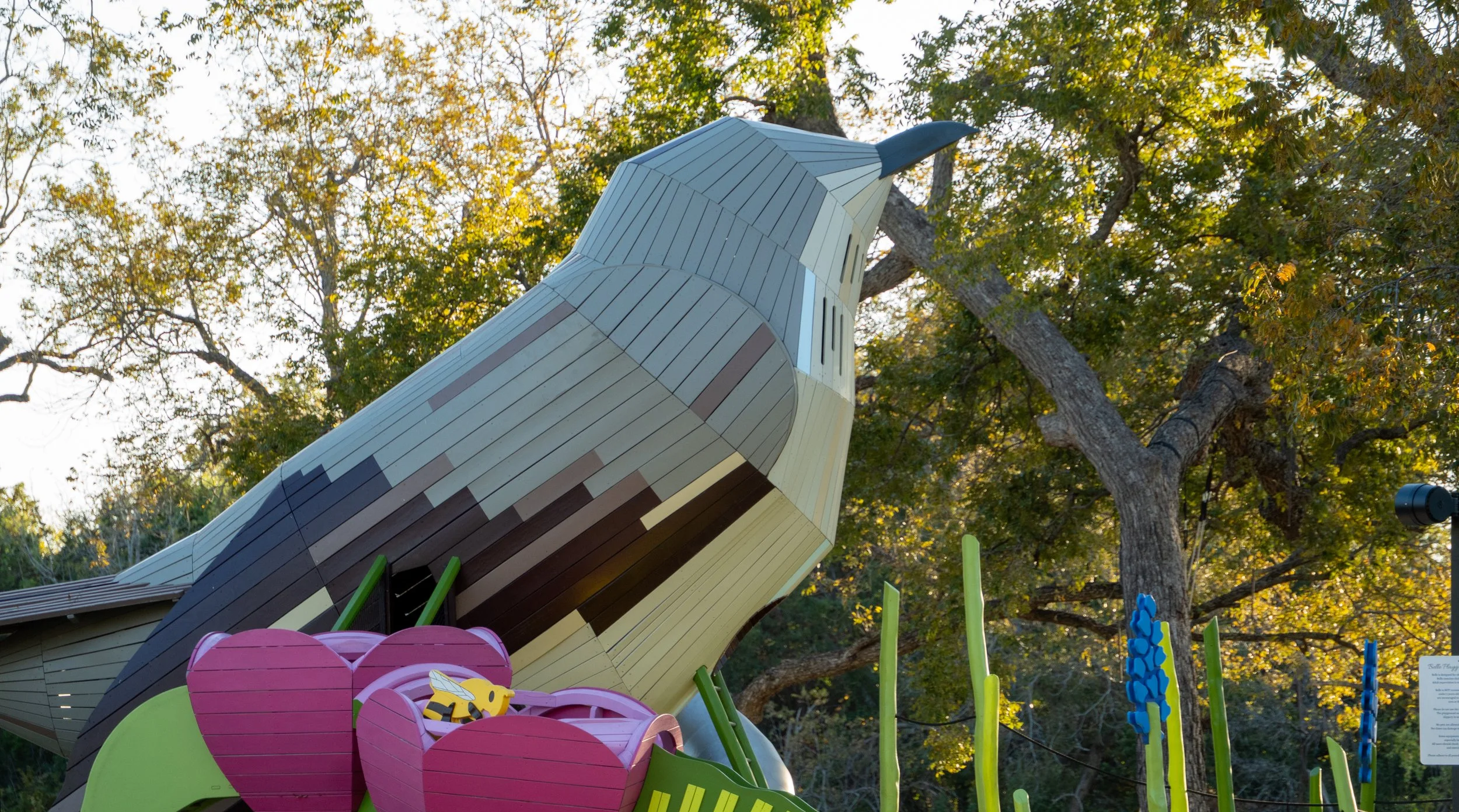 A large, colorful Lego-style sculpture of an eagle with a prominent beak and detailed feathers, set outdoors among trees with autumn foliage.