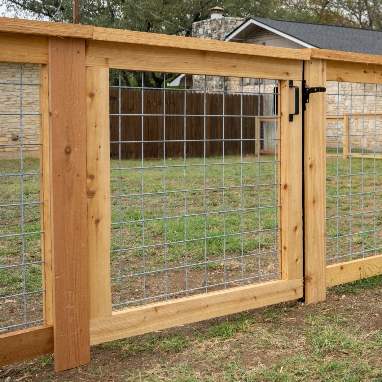 Black metal fence surrounding a garden with green bushes and plants, with a house in the background.