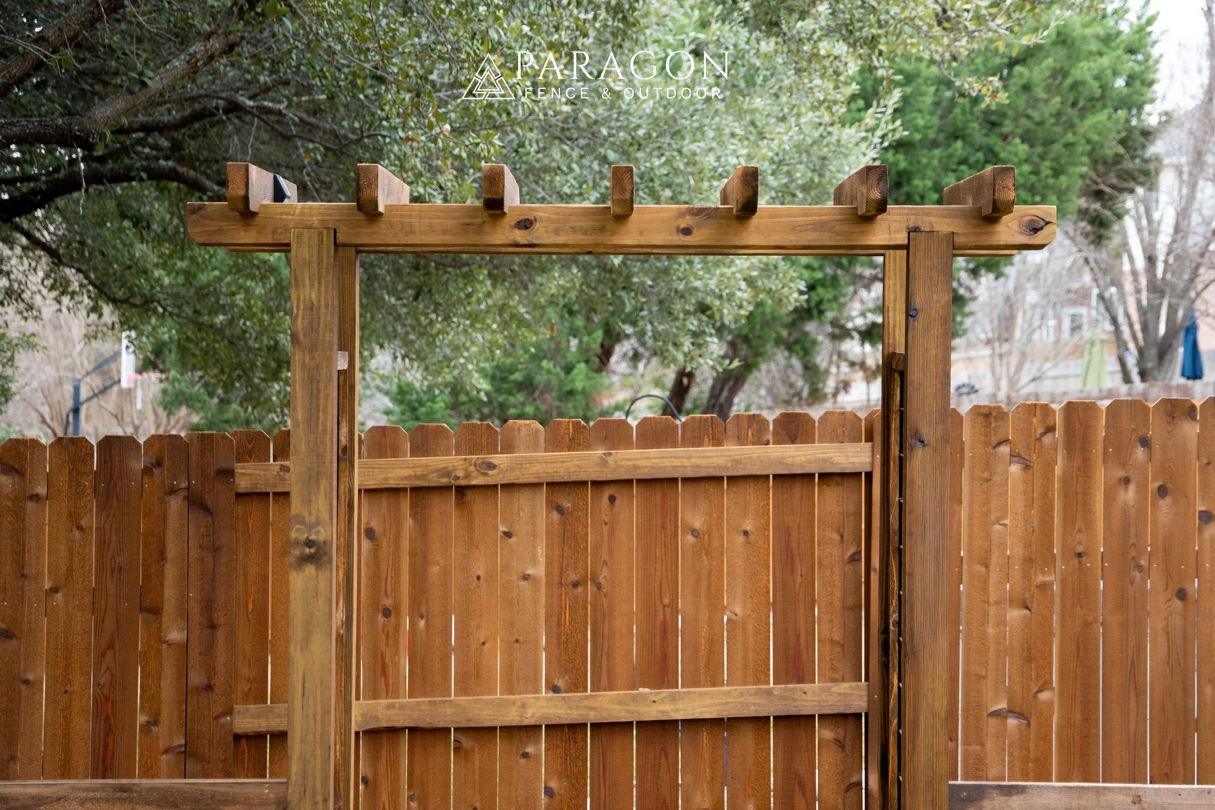 Wooden fence and gate frame in a backyard with trees in the background.