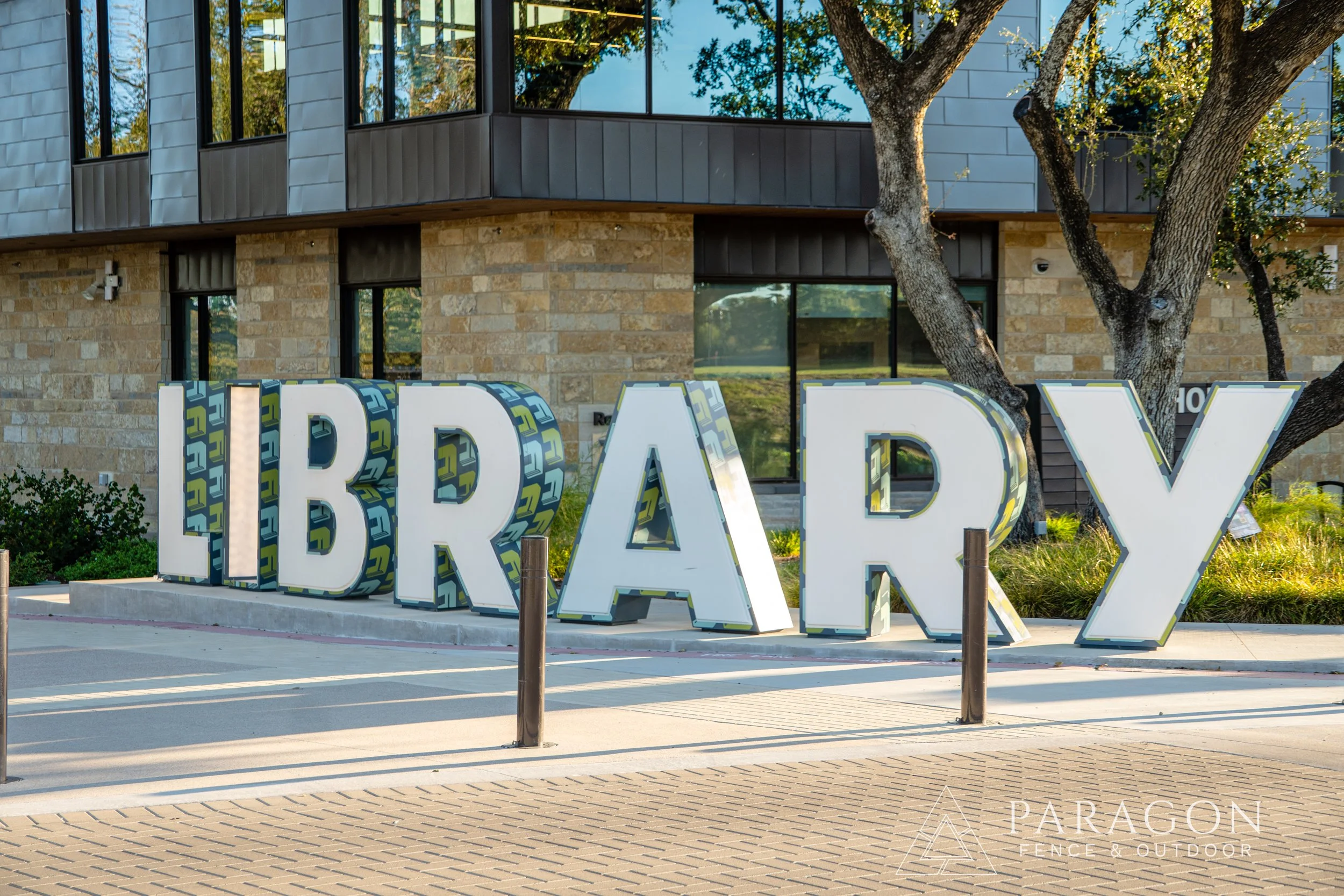 Large illuminated letters spelling 'LIBRARY' outside a modern building with trees and landscaping.