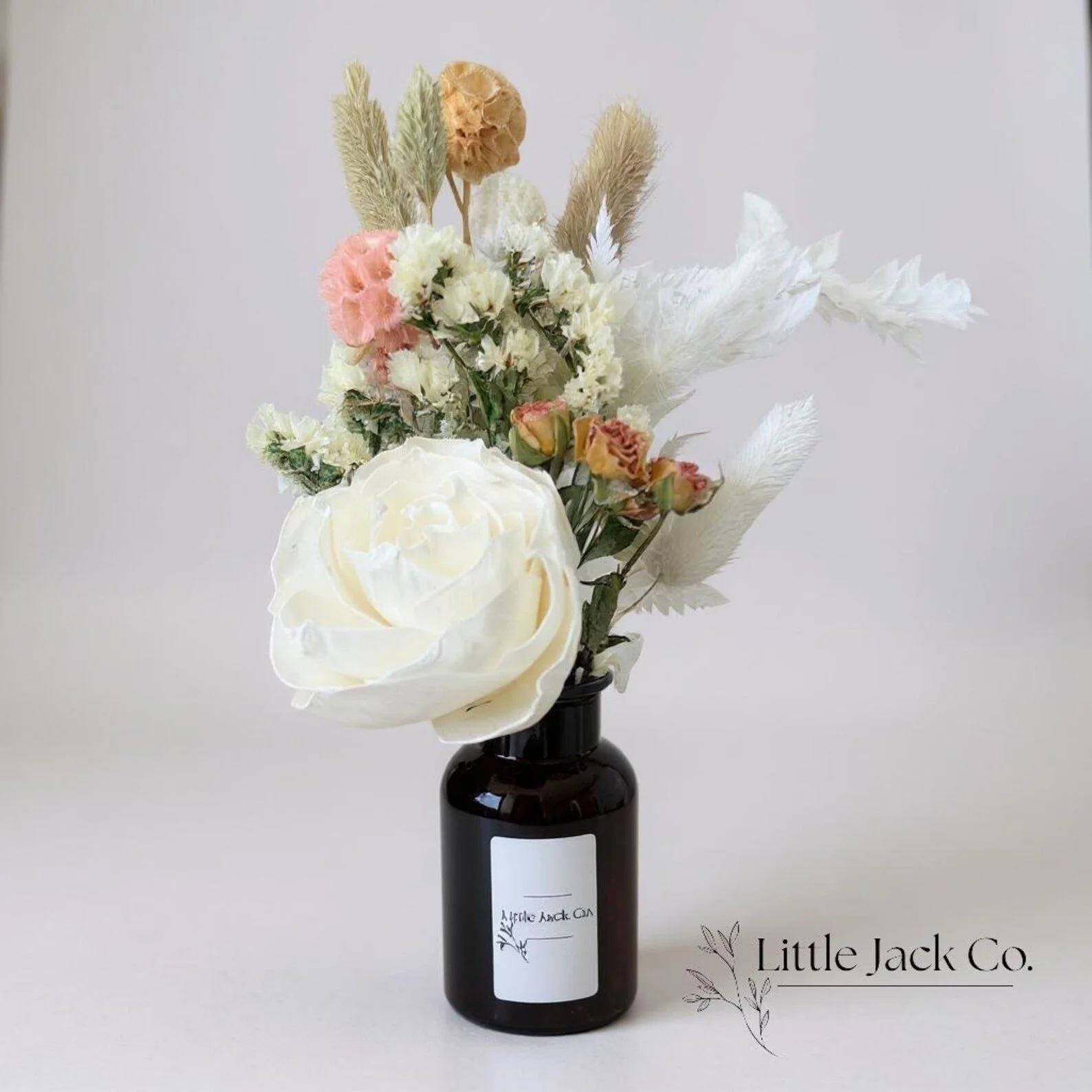 Elegant dried flower arrangement with a white rose, scabiosa, statice, fern and greenery in an amber vase