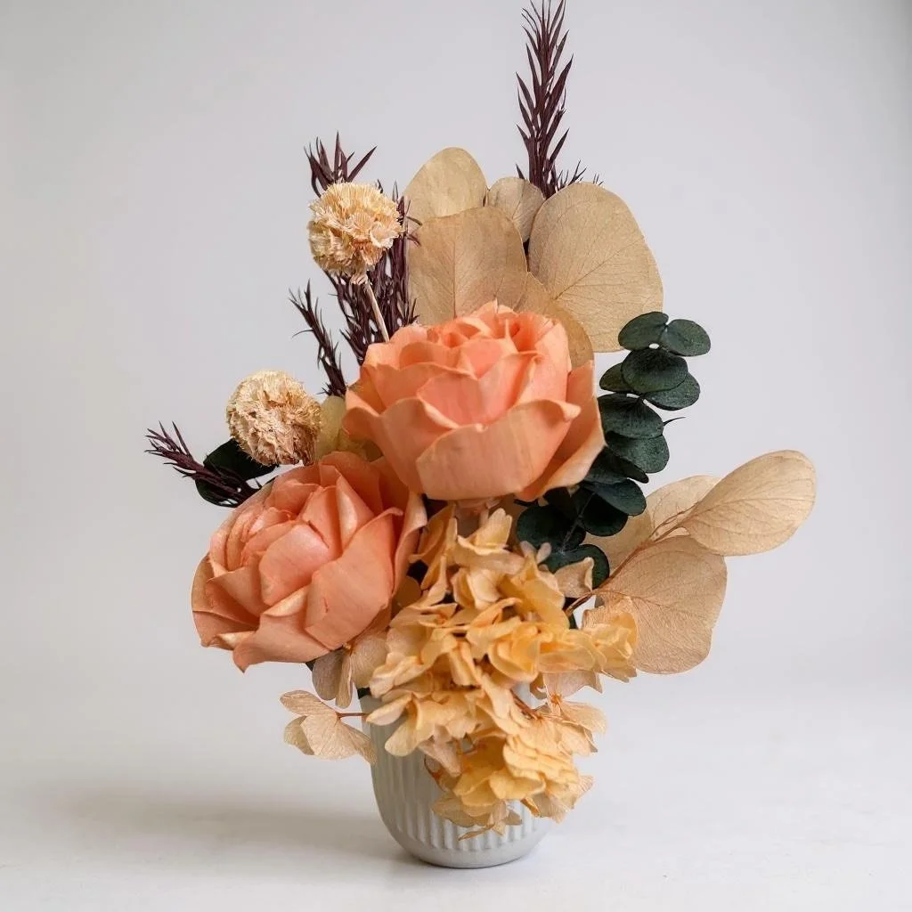 Dried flower arrangement with orange roses, apricot eucalyptus, apricot hydrangea in a ribbed ceramic vase