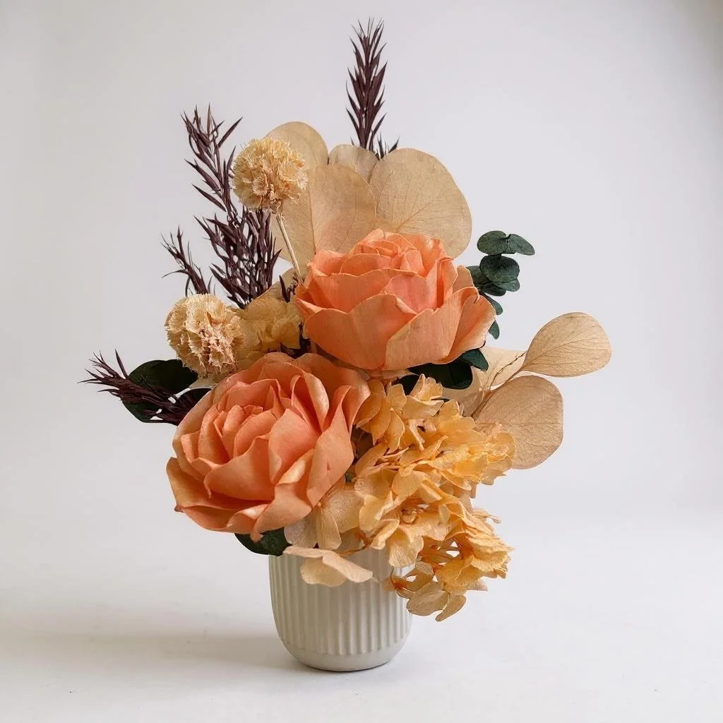 Dried flower arrangement with orange roses, apricot eucalyptus, apricot hydrangea in a ribbed ceramic vase