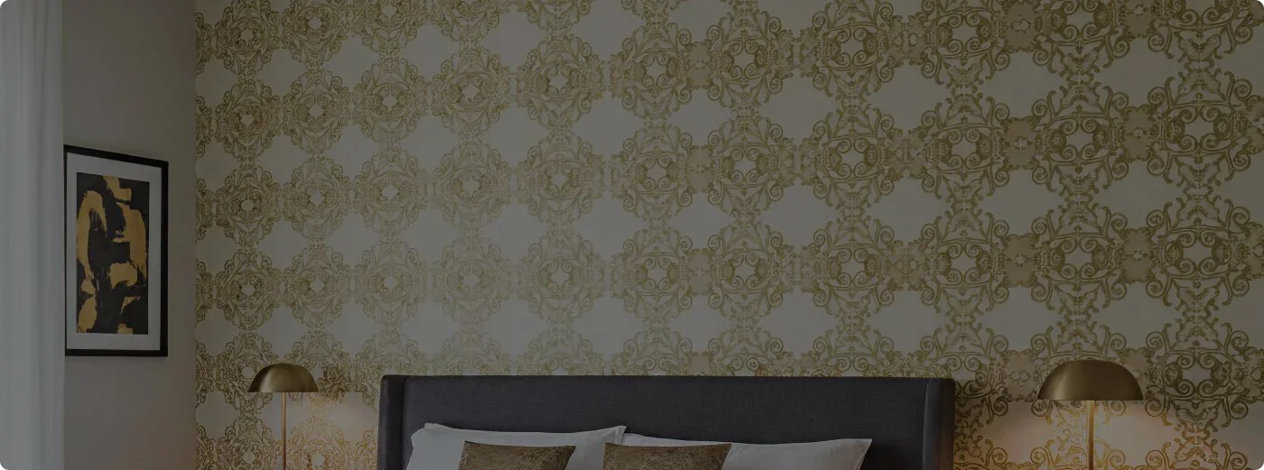 View of a bedroom with a black bed, gold decorative wallpaper, matching gold table lamps, and a wall art piece on the left.