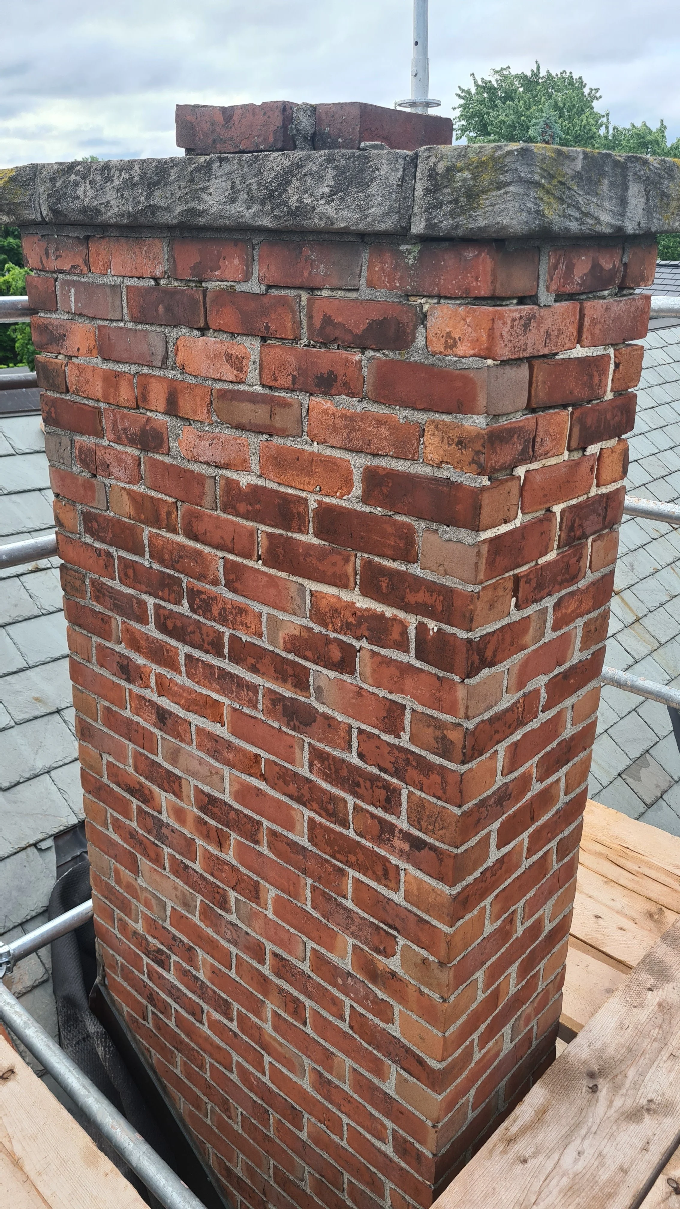 Perfect example of what happens when you use cement incorrectly. The top six courses have been repaired with cementitious mortar, and as a result have caused the bricks to spall and fail, where the original lime mortar remains in good condition. 