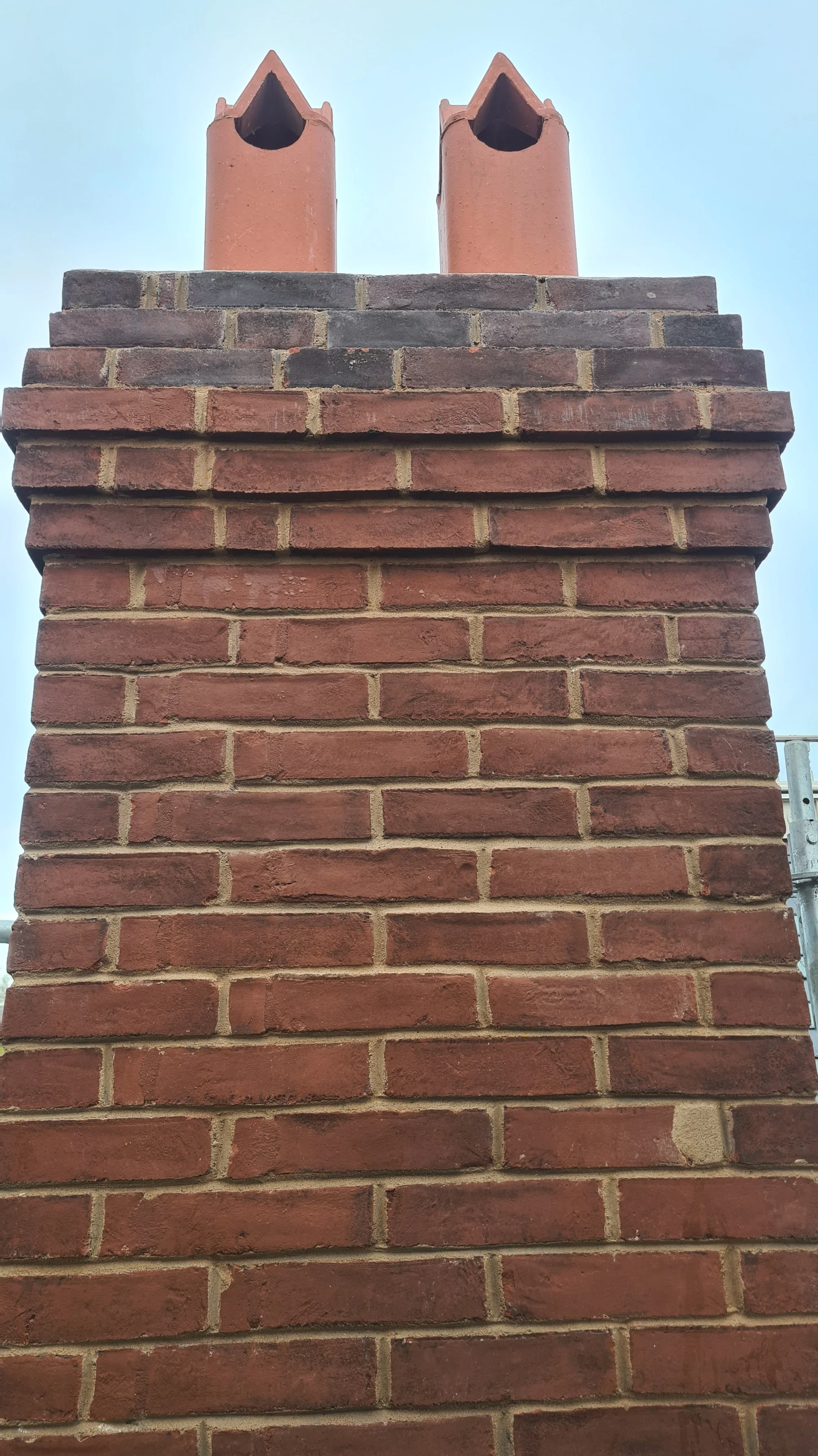 Close-up of a brick chimney with two terracotta chimney pots against a light blue sky.