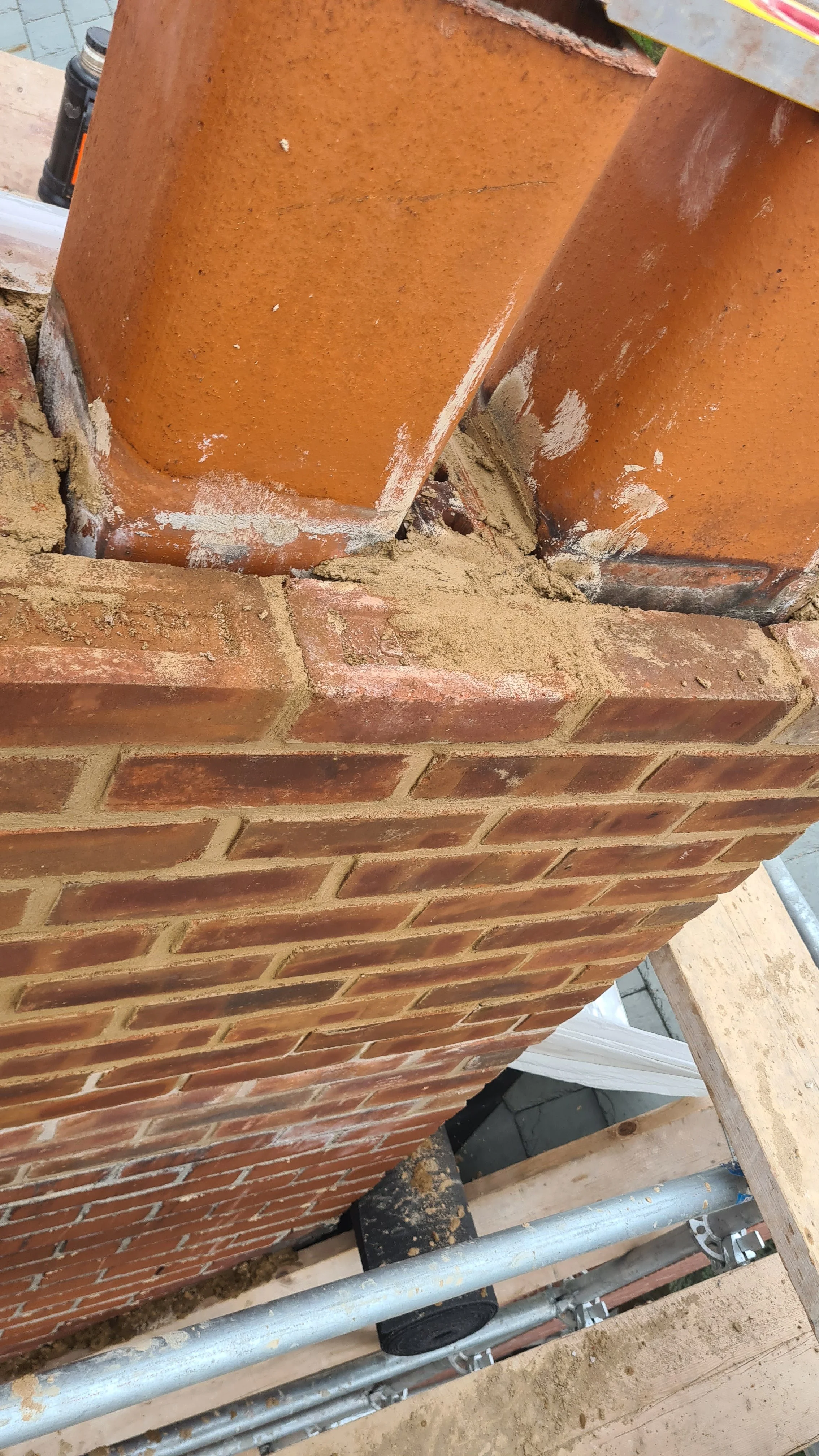 Close-up photo of a brick chimney with mortar working on repairs, scaffolding surrounding it, and construction tools nearby.