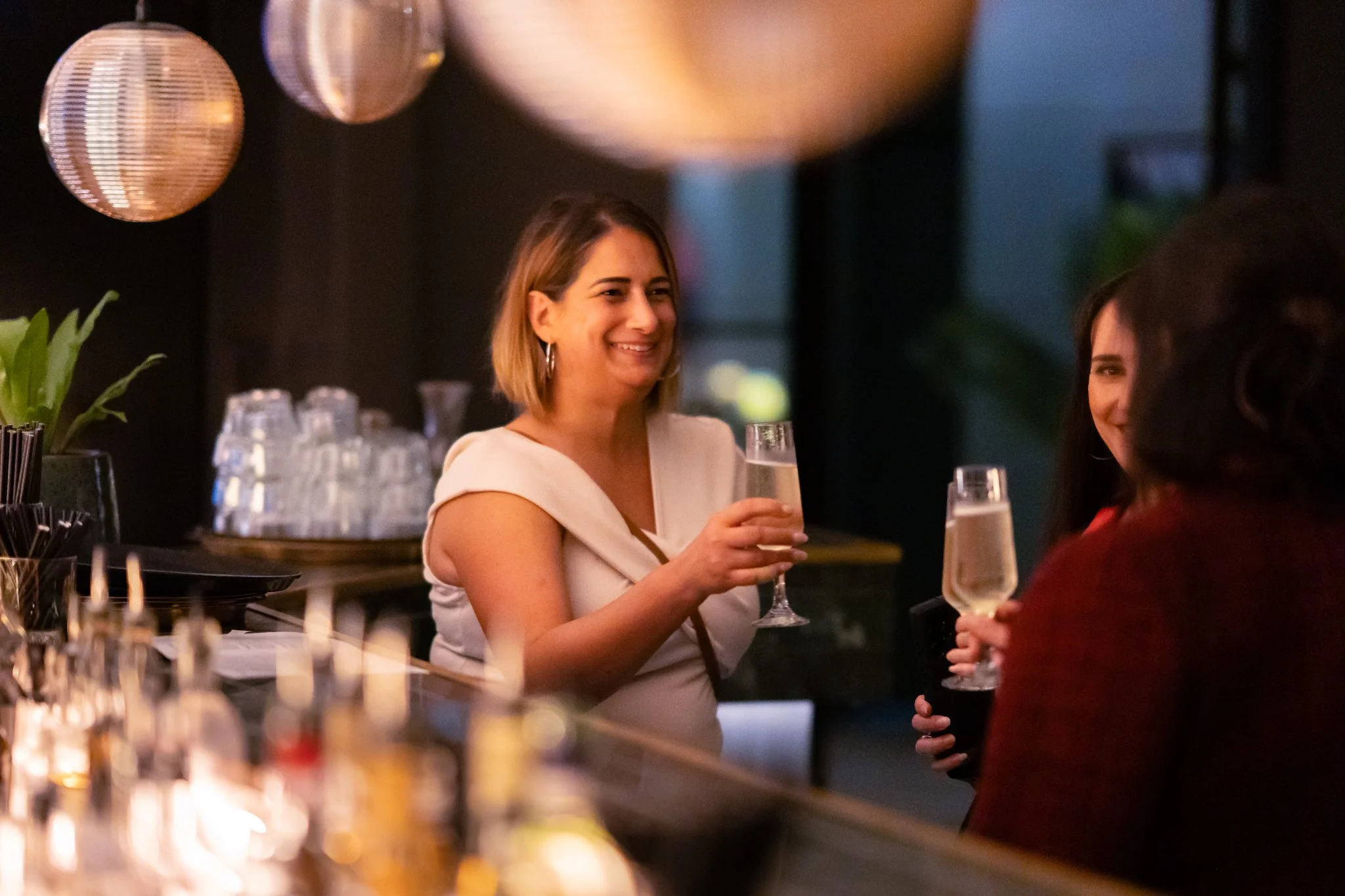 Women socializing at a bar, holding glasses of champagne, smiling and engaging in conversation.