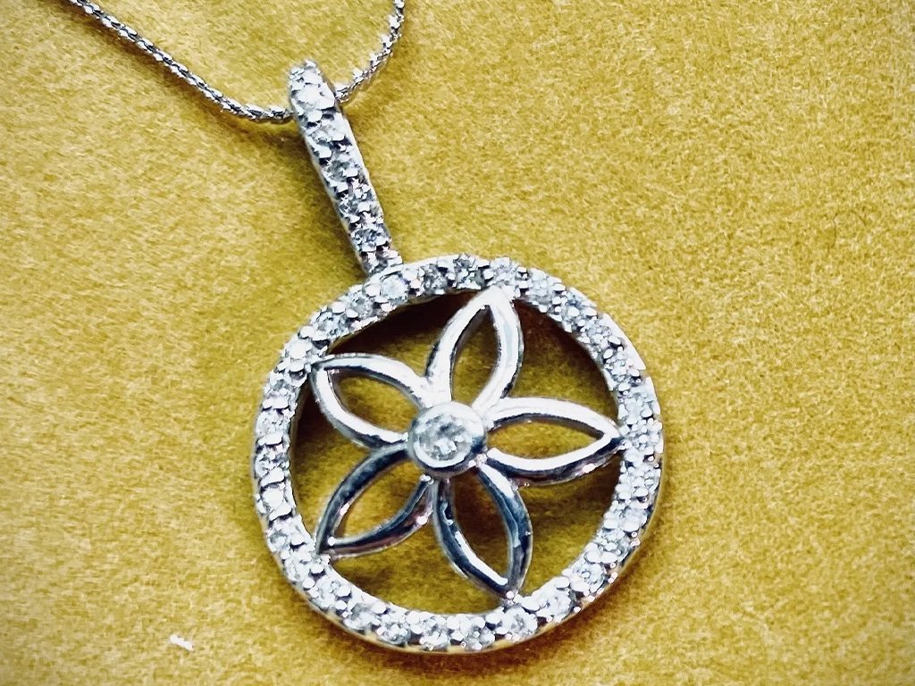 Silver necklace with a circular pendant featuring a flower design, surrounded by small gemstones, on a yellow background.