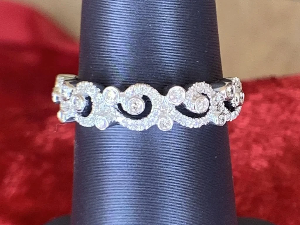 A diamond ring with a swirling, intricate design, displayed on a black stand with a red textured background.