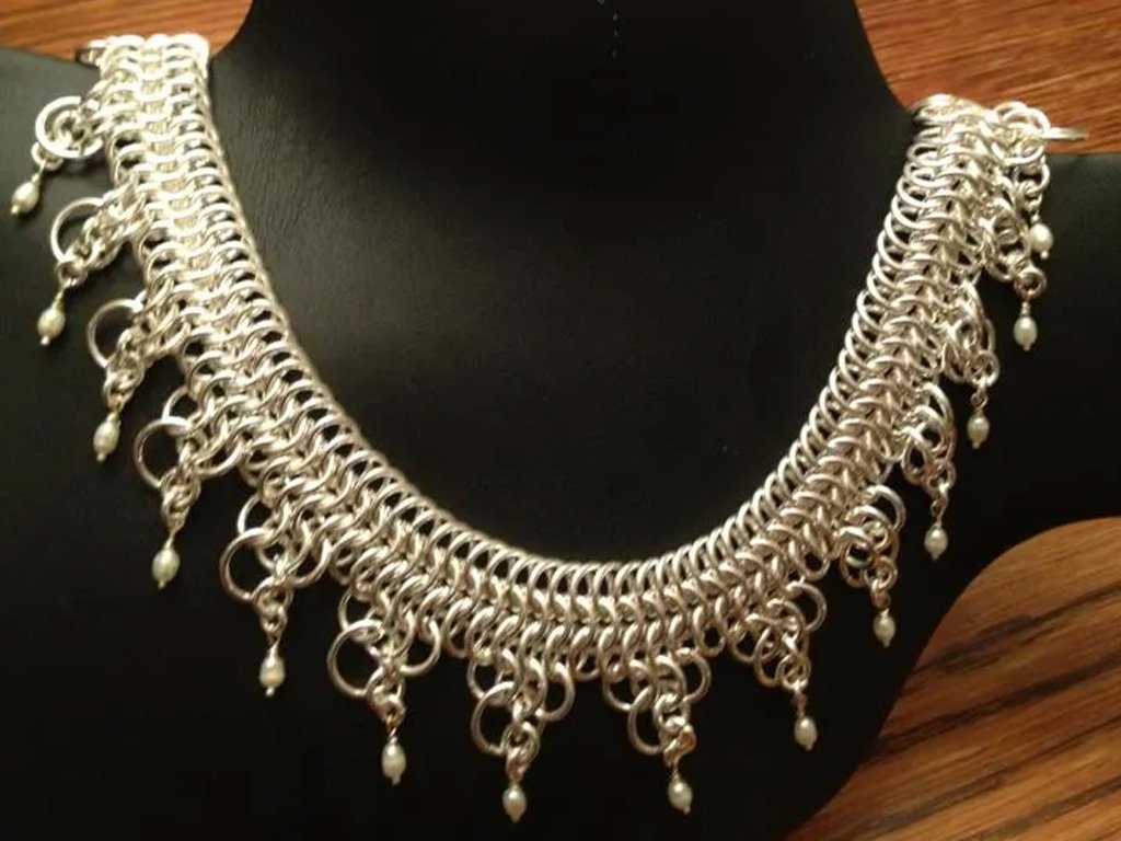 Silver statement necklace with chain links, decorative rings, and pearl accents displayed on a black bust stand.