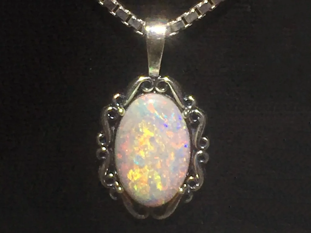 Silver pendant necklace with an oval opal gemstone on a black background.