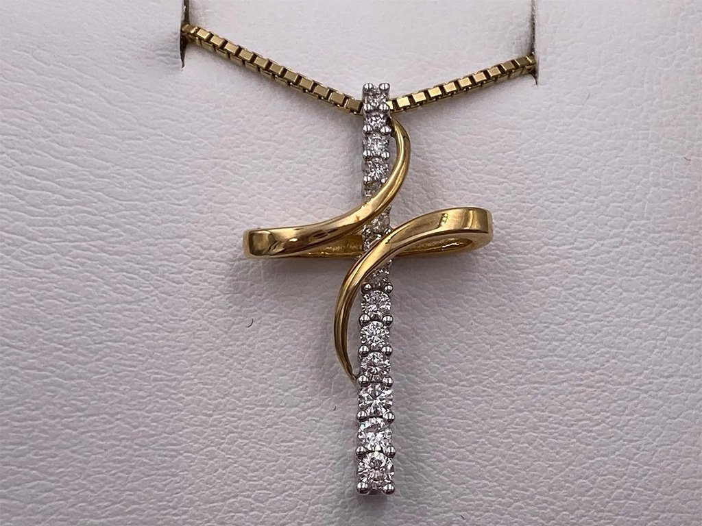 Gold and silver cross-shaped pendant with embedded diamonds hanging from a chain