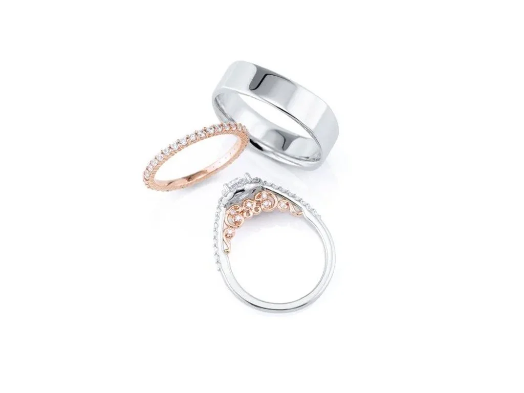 Set of three rings: a plain silver band, a rose gold band with small diamonds, and a silver ring with pink and clear stones.